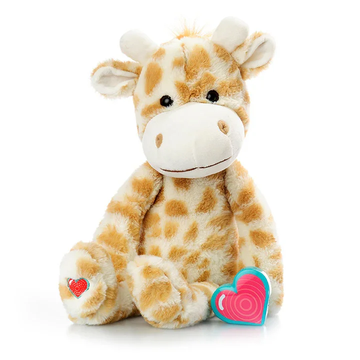 Soft plush giraffe toy with a white face and orange spots, sitting on a white background, with a colorful heart-shaped box in front and a small heart patch on its paw.