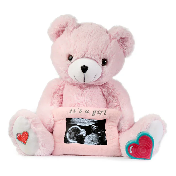 Pink plush teddy bear holding an ultrasound picture with text "It's a girl" and heart decorations.