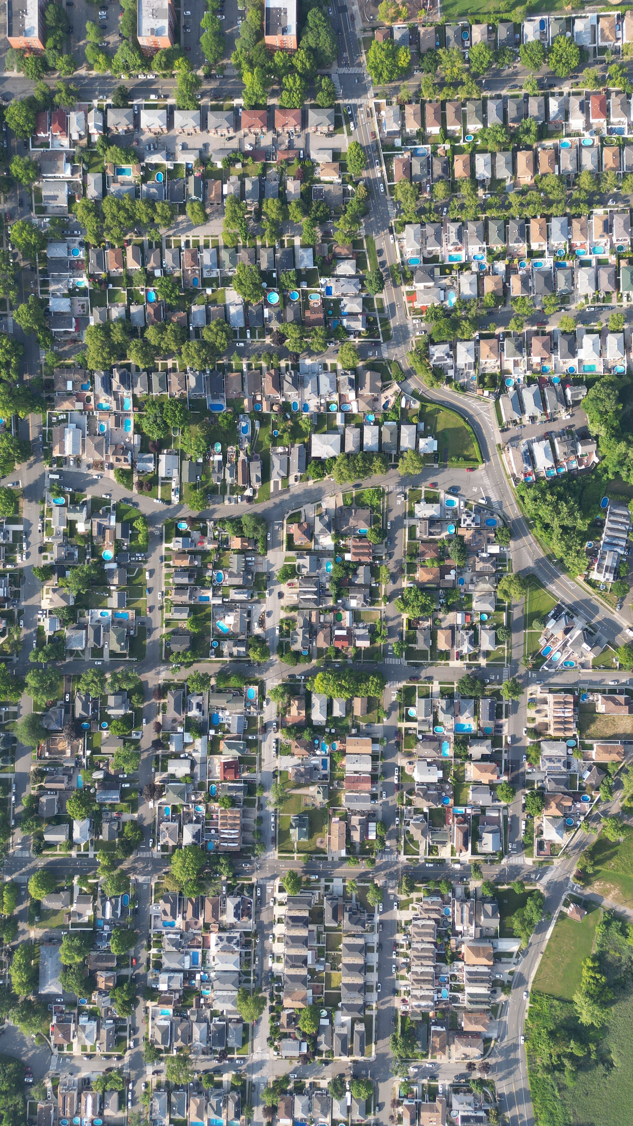An aerial view of a residential neighborhood with houses, trees, and streets, many with blue pool covers in backyards.
