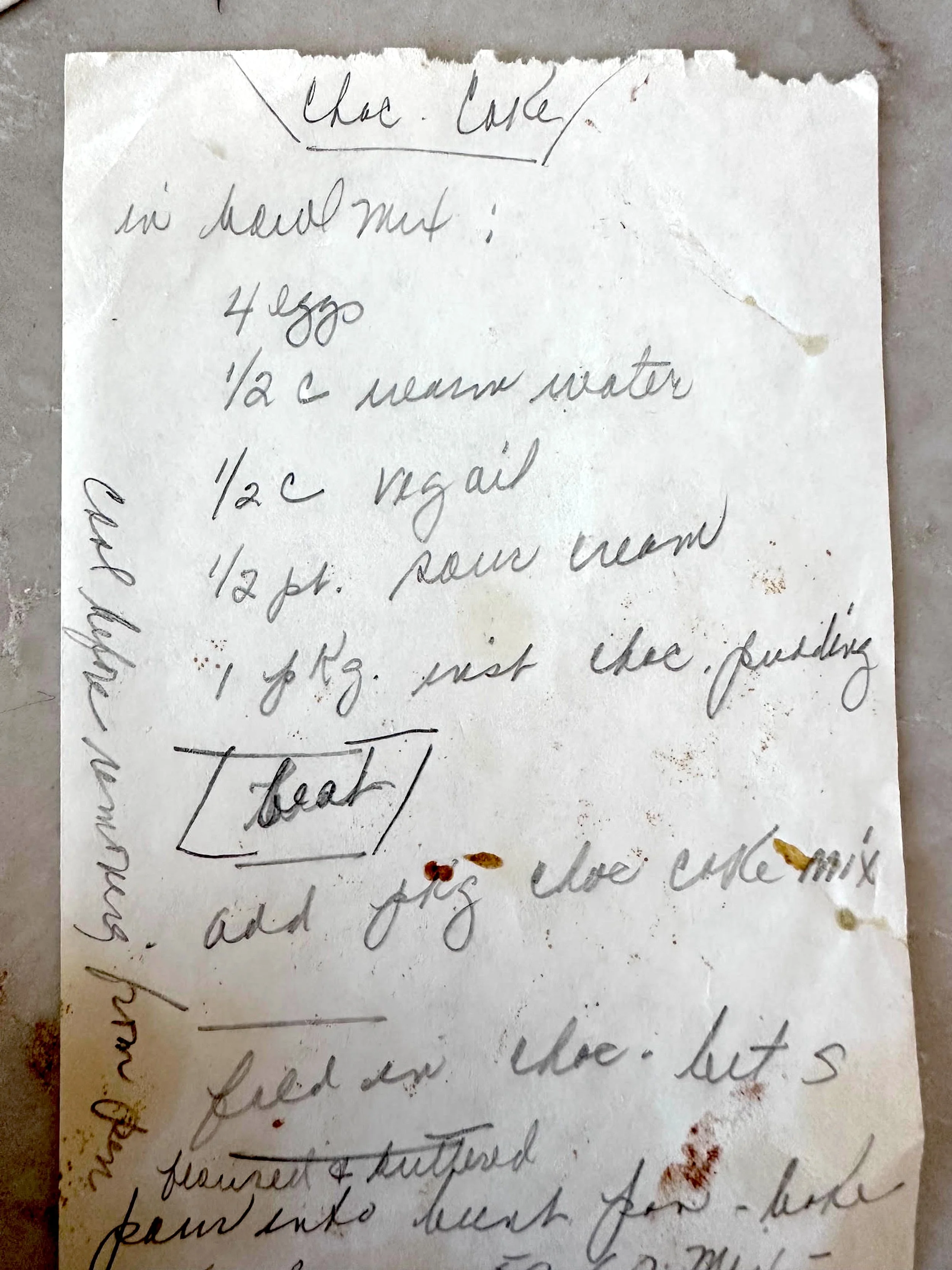 A worn, food-stained scrap of paper bearing a handwritten recipe in looping cursive, with torn edges and crossed-out notes.