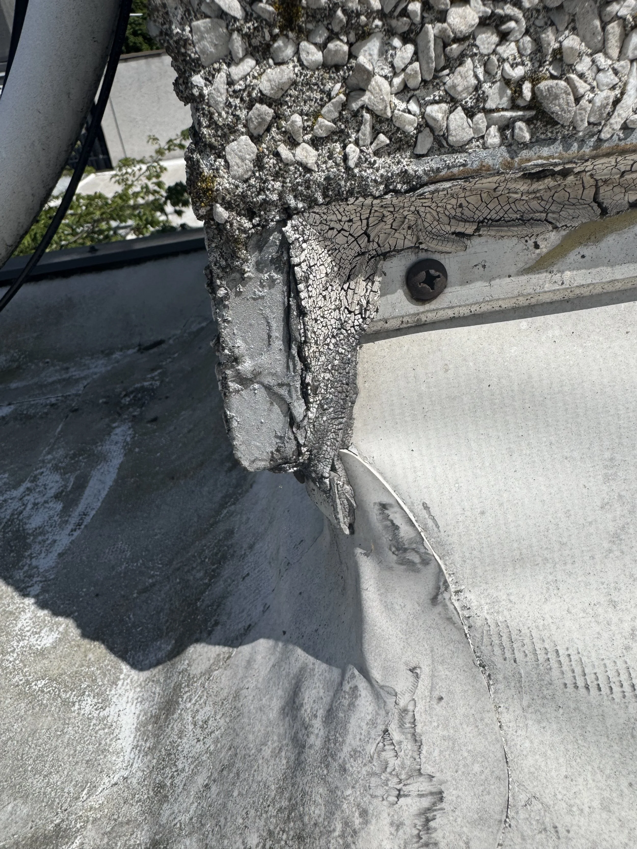 Close-up of a damaged section on a building's exterior, showing cracked and peeling paint, a partially exposed screw, and concrete with signs of weathering and deterioration.