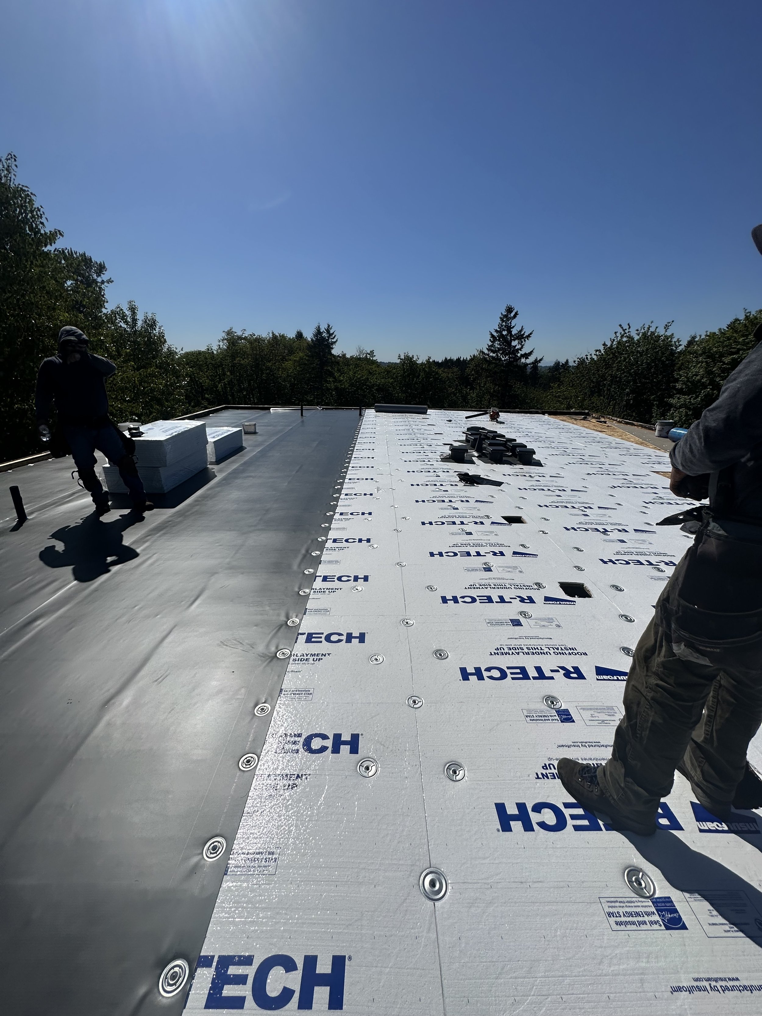 Construction workers installing roofing insulation on a building roof under a clear blue sky.