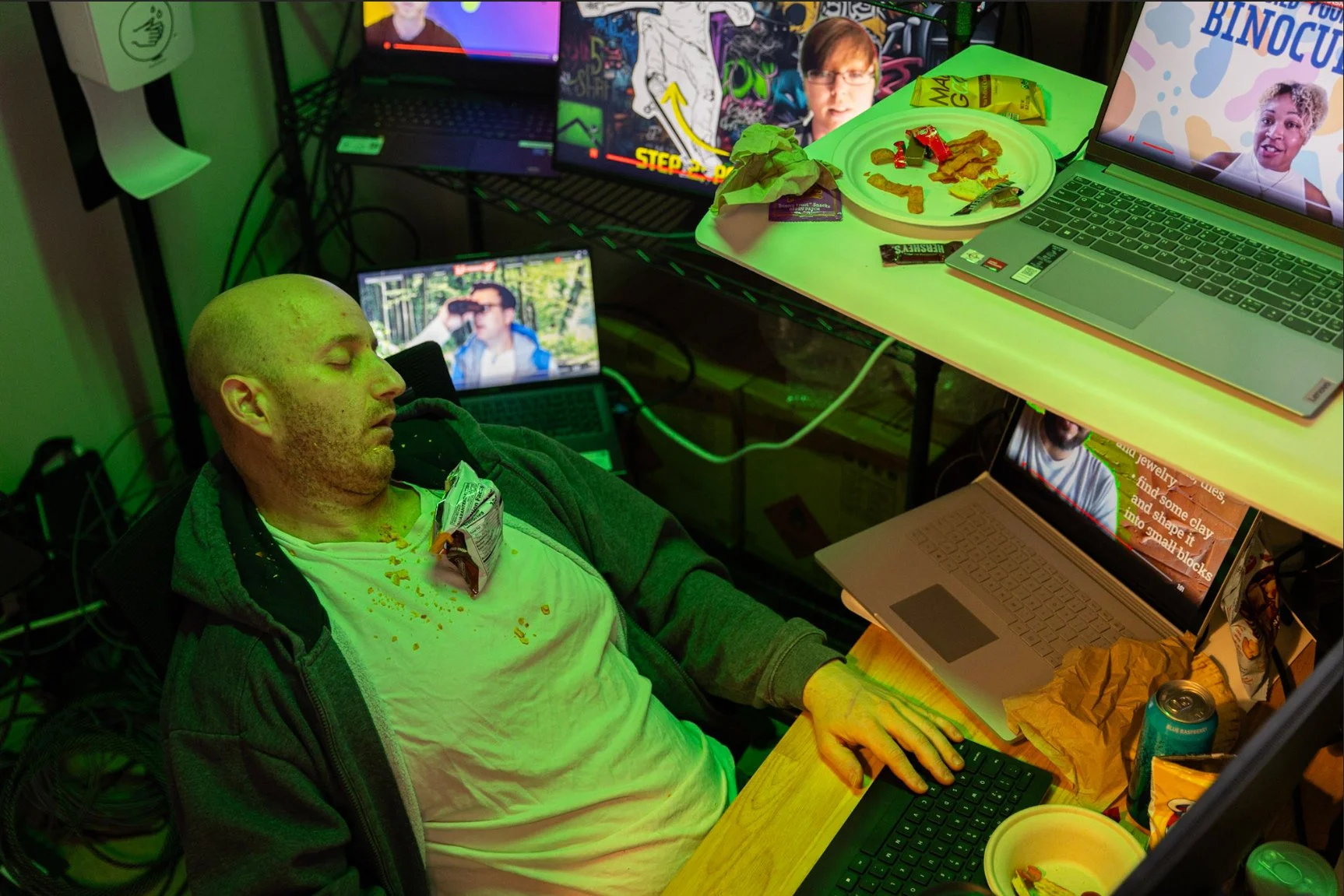 A man sleeping at a desk with a computer and food on his chest