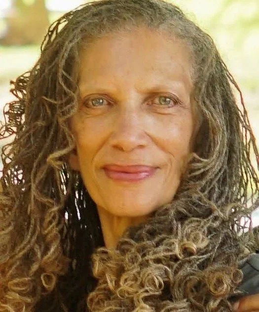Close-up of a woman with curly hair smiling outdoors.