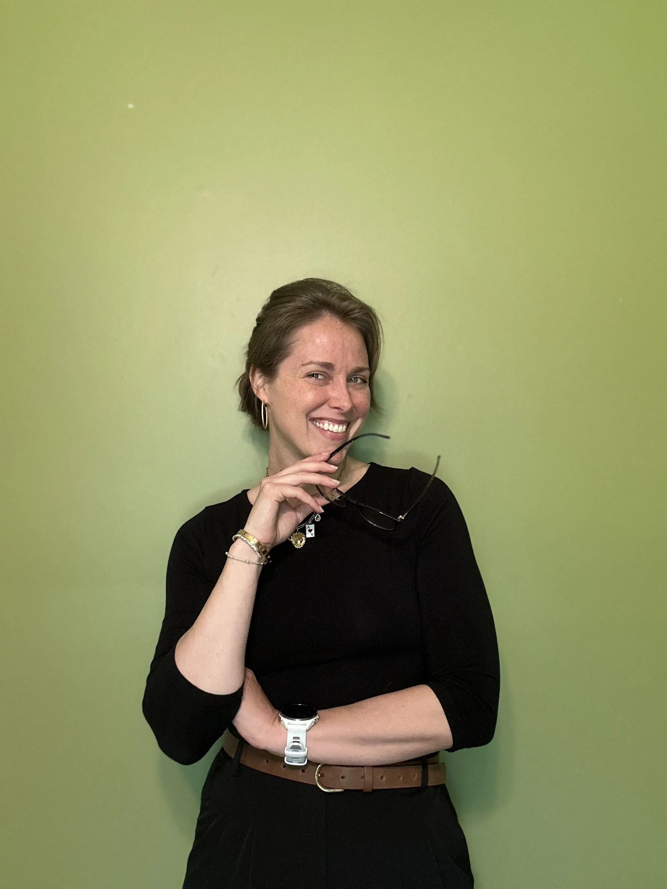 JoHanna Abell, Wellness Coach, standing in an inviting posture with glasses in her right hand and smiling.