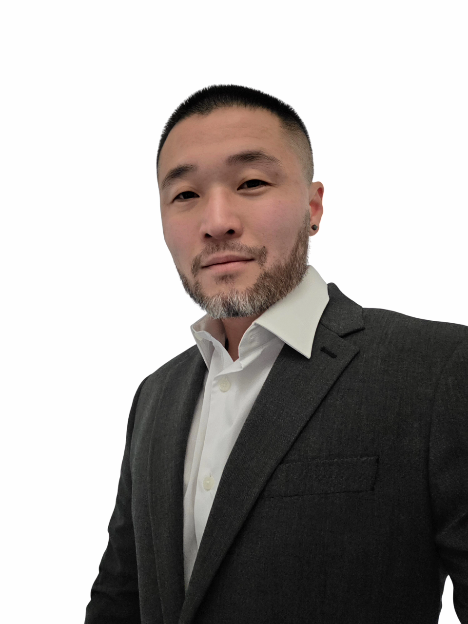 A man wearing a dark suit and white shirt, with short black hair and facial hair, posing in front of a plain white background.
