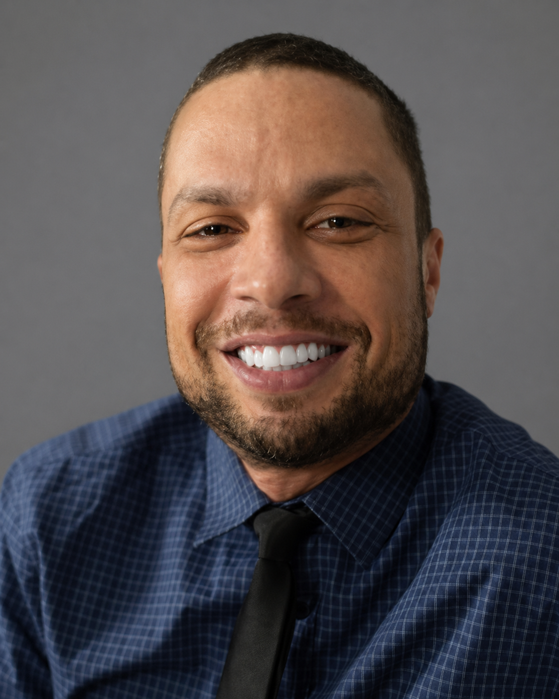 Headshot of Jason Rosa, a licensed therapist specializing in couples, anxiety and trauma in New Jersey, wearing a blue checkered shirt and smiling warmly against a gray background