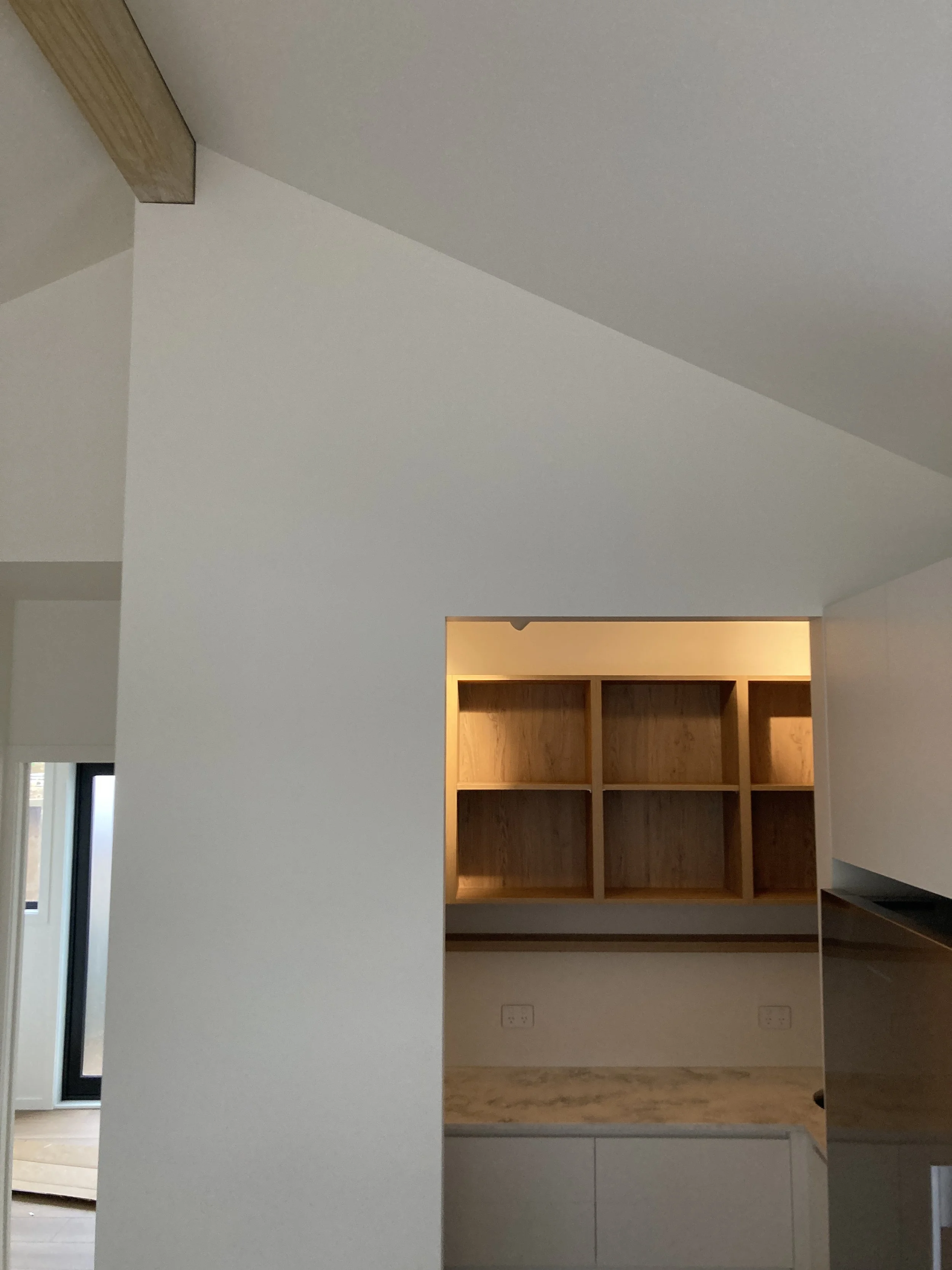 Interior view of a modern kitchen with white cabinets, a marble countertop, and open wooden shelves on a wall, with a glimpse of a sliding glass door to the outside.