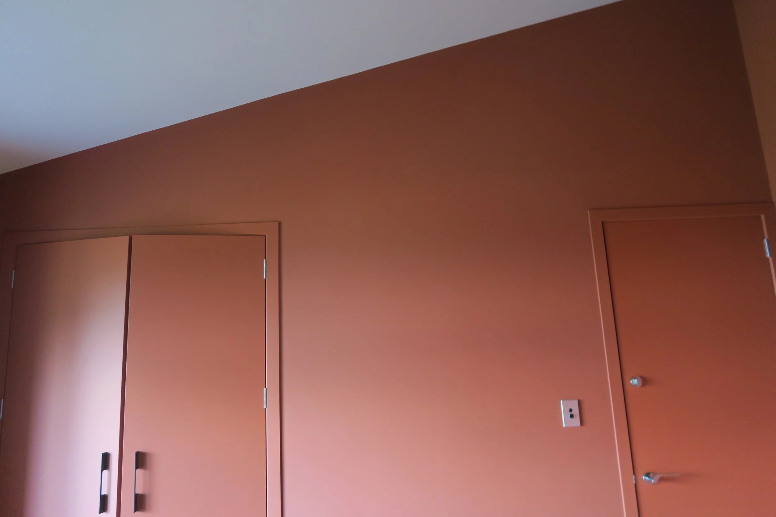Interior wall with closed brown closet doors, an electrical outlet, and a brown door with a metallic doorknob, all against a matching brown wall.