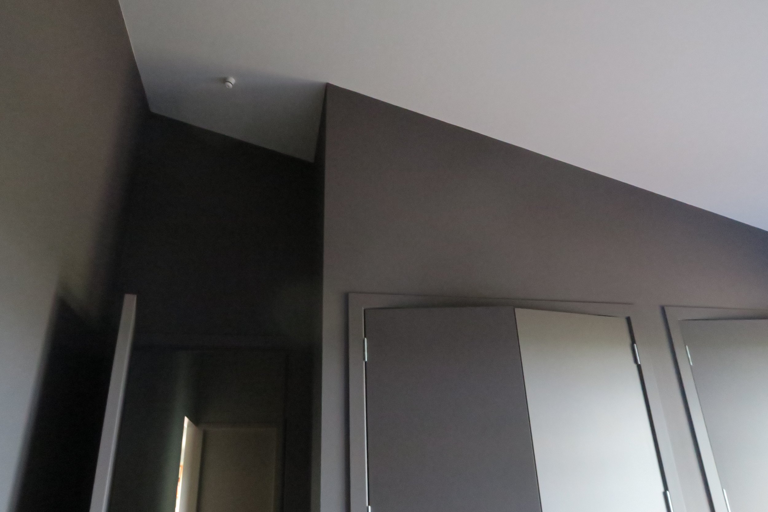 Interior of a modern room with gray walls and a white ceiling, featuring closed gray closet doors and a narrow doorway with a light visible through it.