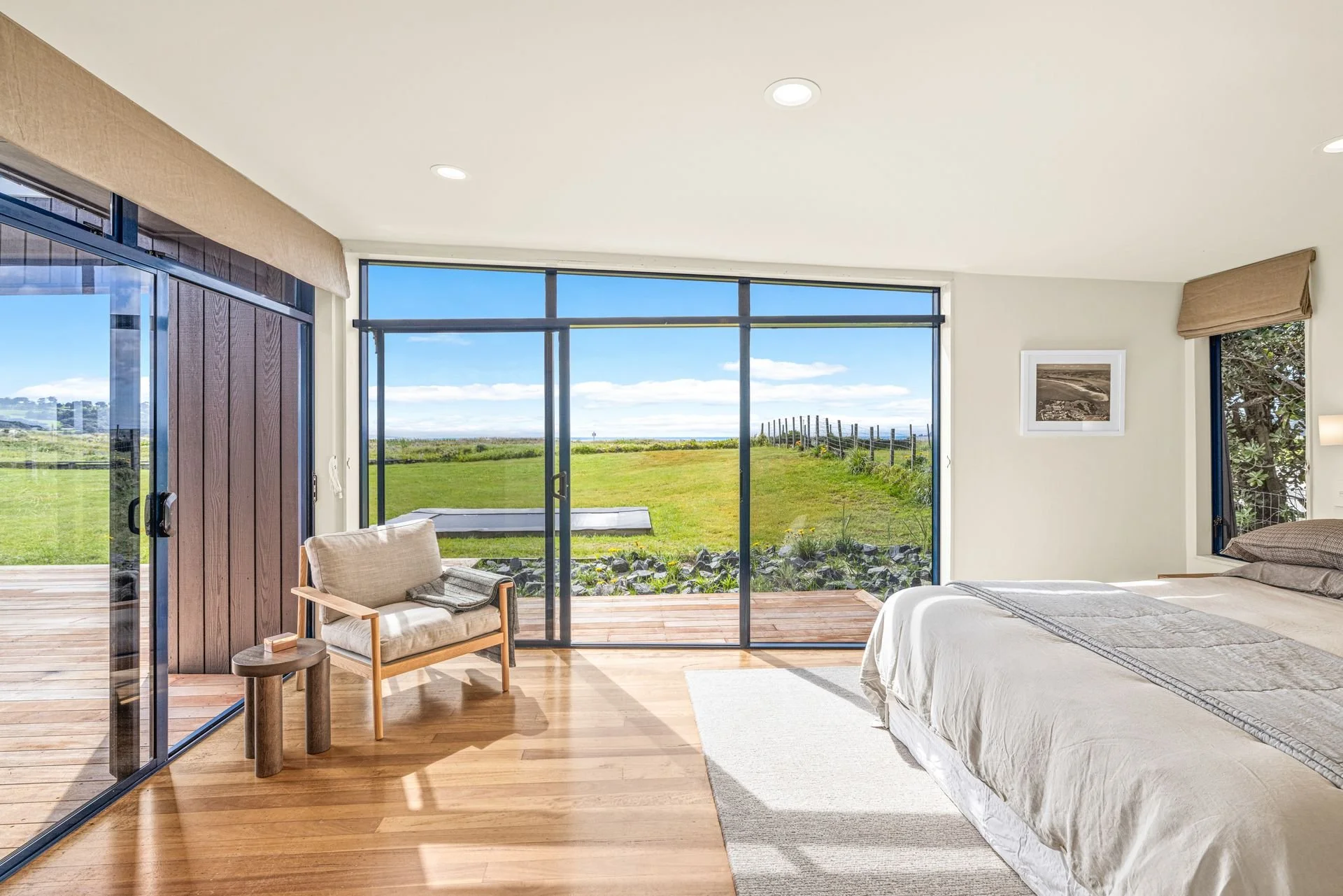 A bedroom with a large glass sliding door leading to a deck and a grassy outdoor area on a sunny day.
