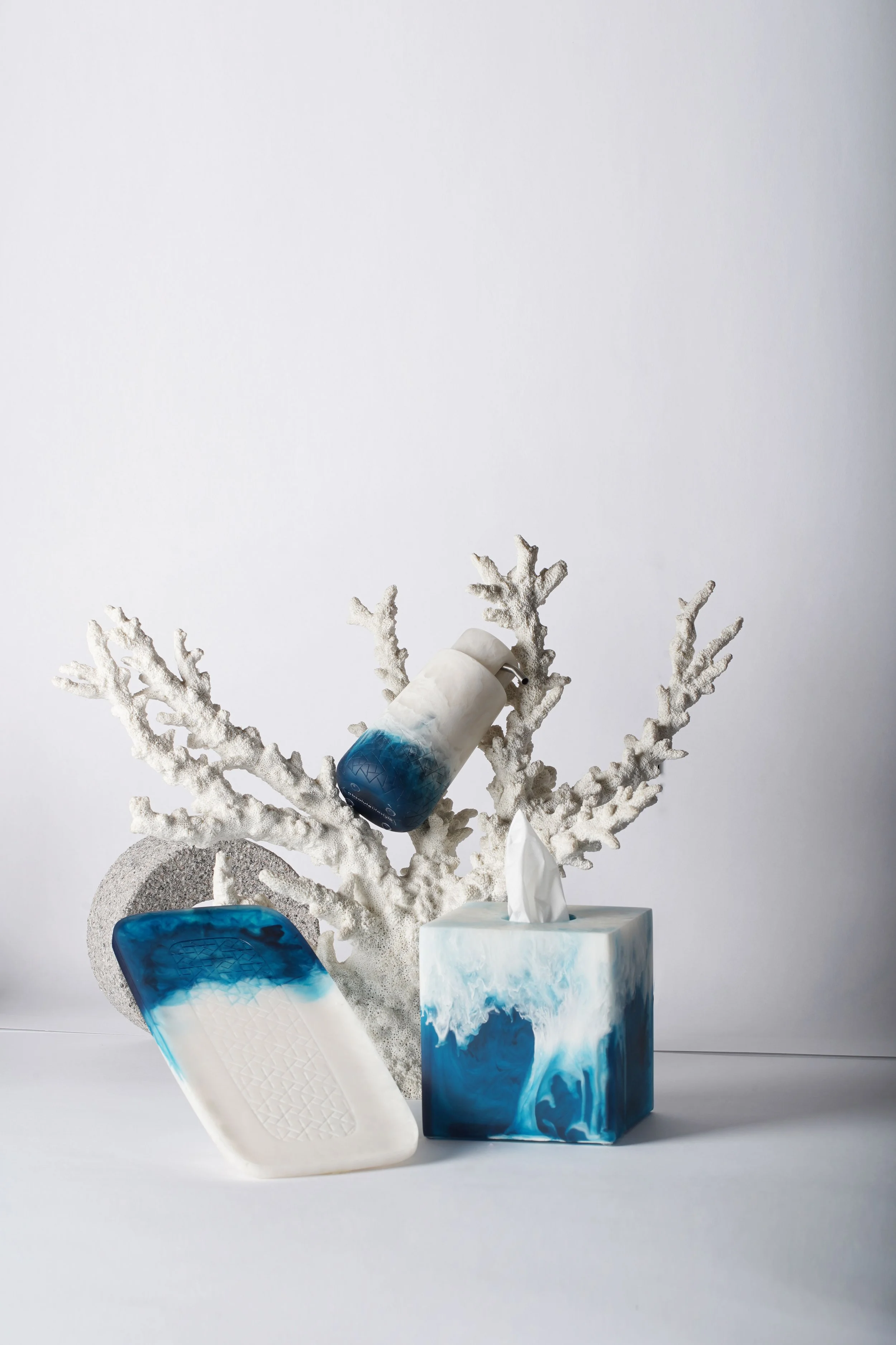Decorative items including a tissue box, a soap or lotion dispenser, a tray, and a white coral branch arrangement, all with a blue and white marble design, against a plain white background.