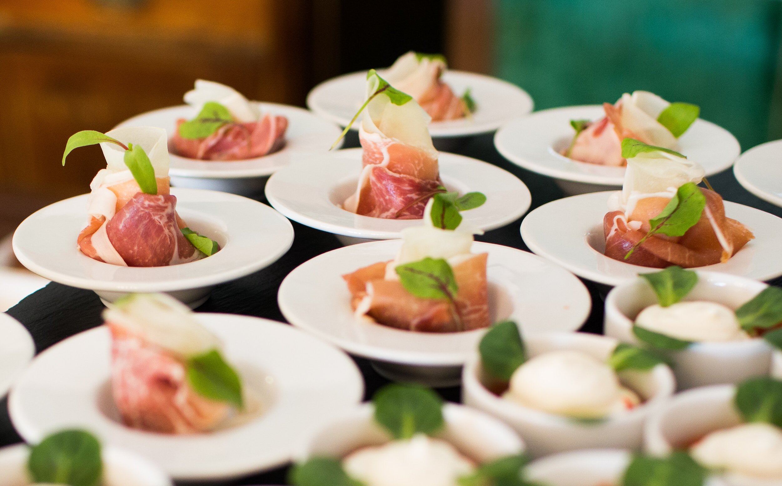 Petites assiettes de jambon cru roulé avec des pousses vertes en garniture.