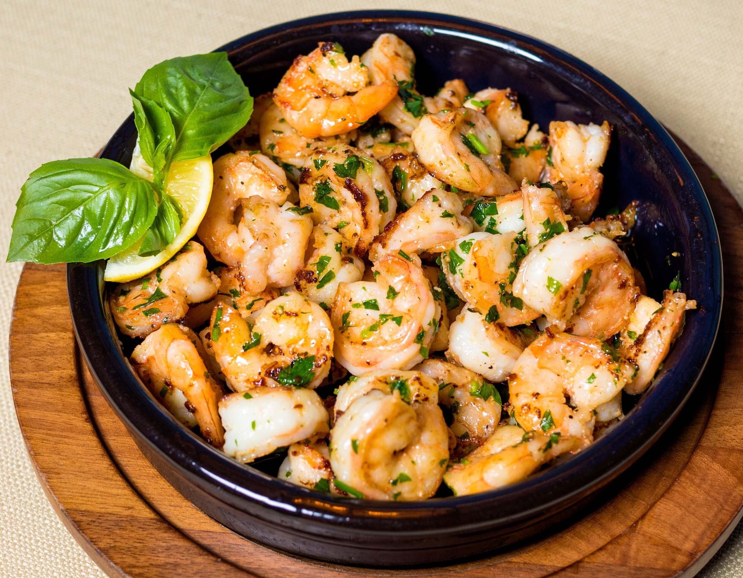 Crevettes grillées avec herbes et citron dans un bol noir, garni de feuilles de basilic.