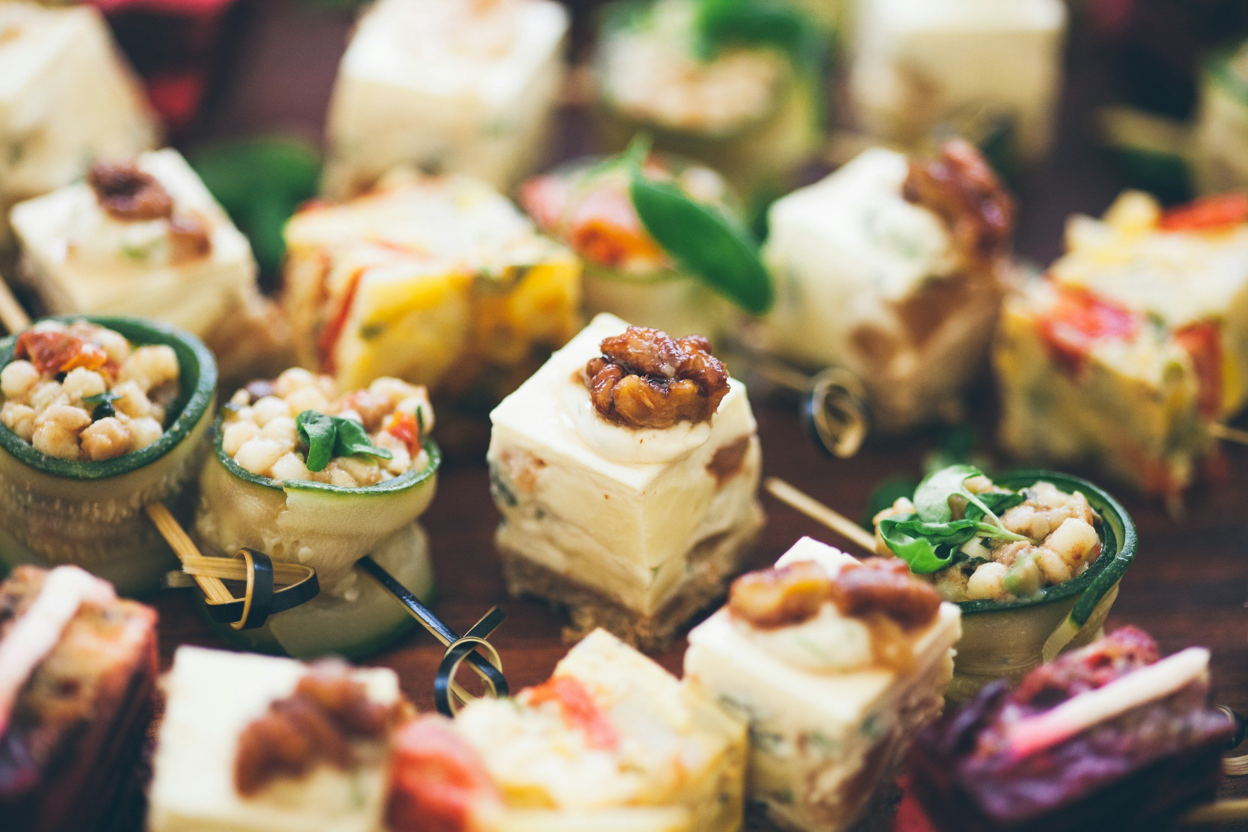 Variety of gourmet hors d'oeuvres and canapés présentés sur une table, comprenant des petites bouchées avec fromage, légumes et garnitures.