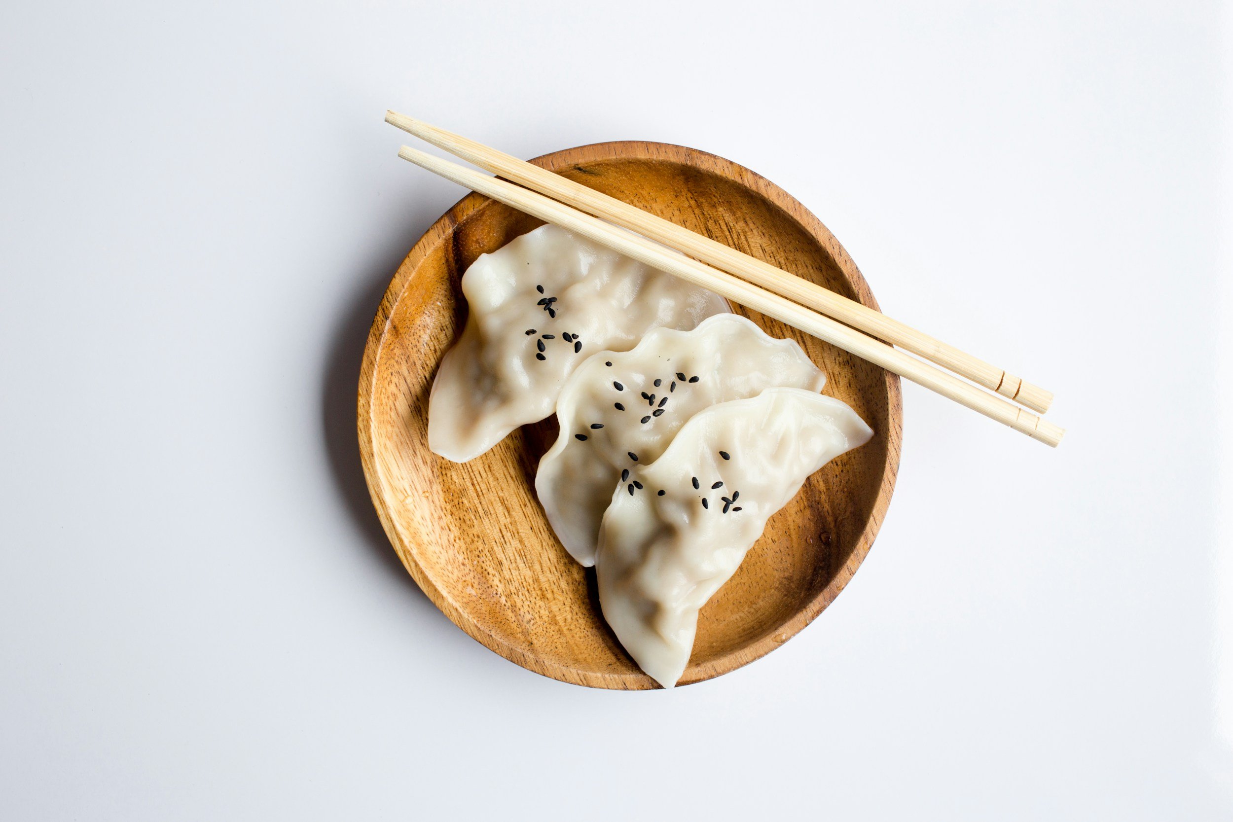 Trois raviolis garnis dans un bol en bois, garnis de graines de sésame, avec des baguettes posées dessus.