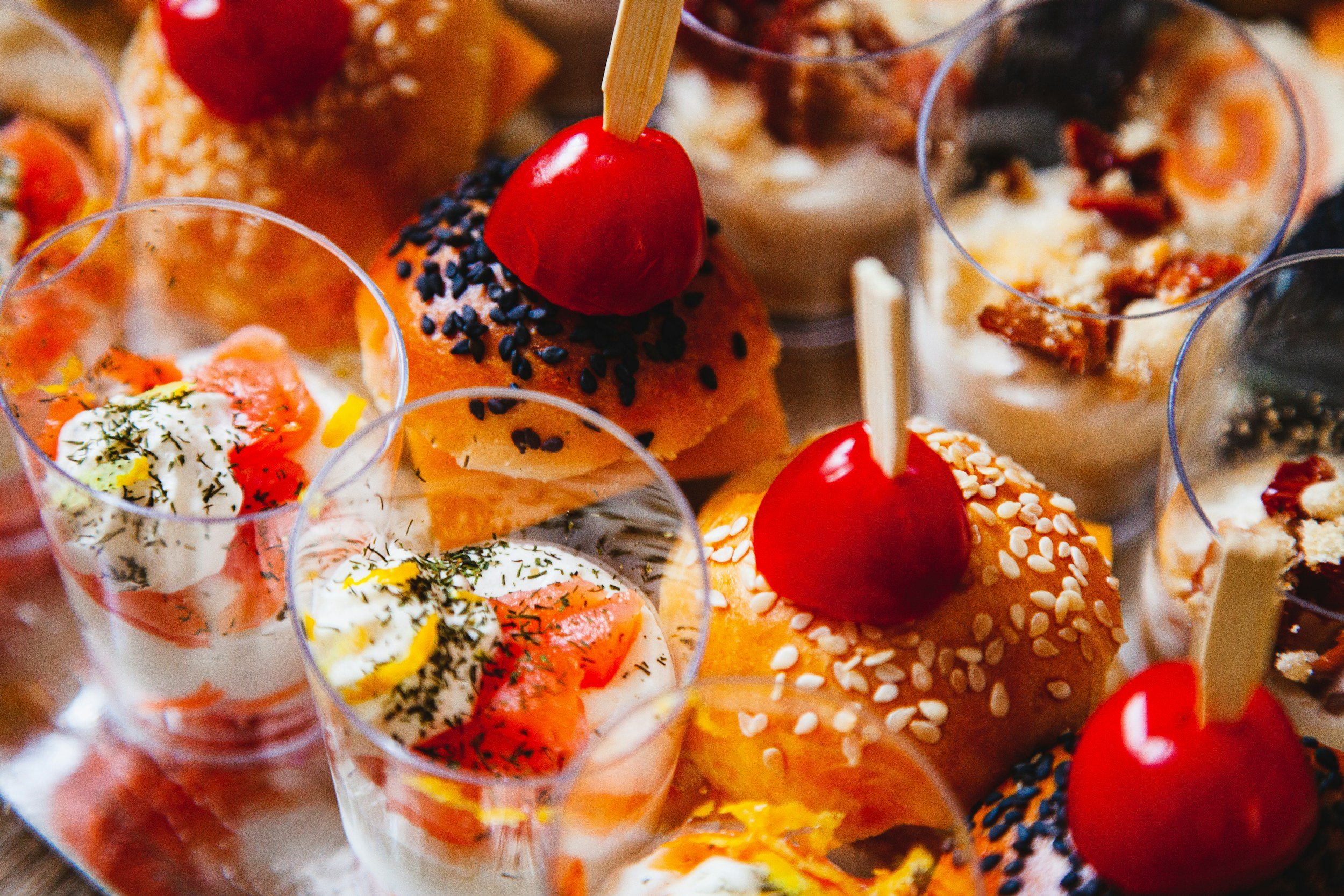 Assortiment de verrines et petites bouchées salées et sucrées, avec des mini sandwichs garnis de crème, poisson, œufs, et des desserts comme des tiramisus avec des biscuits et des fruits.