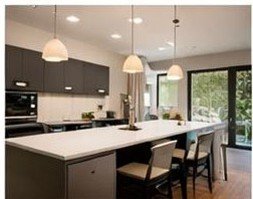 A modern kitchen with dark cabinets, a large island, pendant lights, and a sliding glass door leading outside.