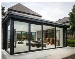 A modern glass sunroom attached to a house, with sliding glass doors and a view of the backyard with green grass and trees.