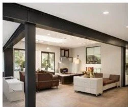 Living room with sofas, armchairs, large windows, and a white wall with framed pictures.