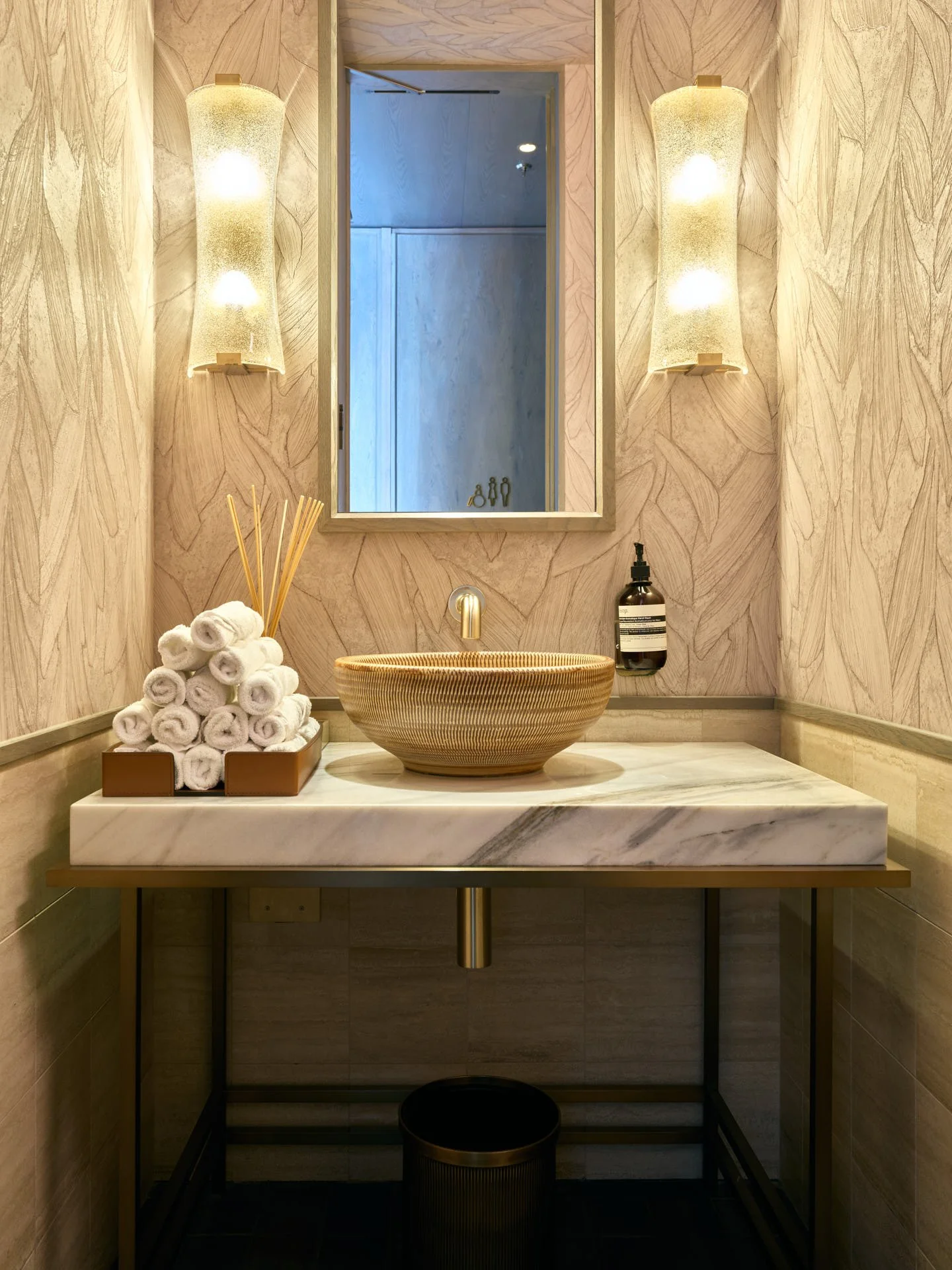 Restaurant restroom with a white marble vanity, bronze bowl basin, patterned wall finish and warm lighting.