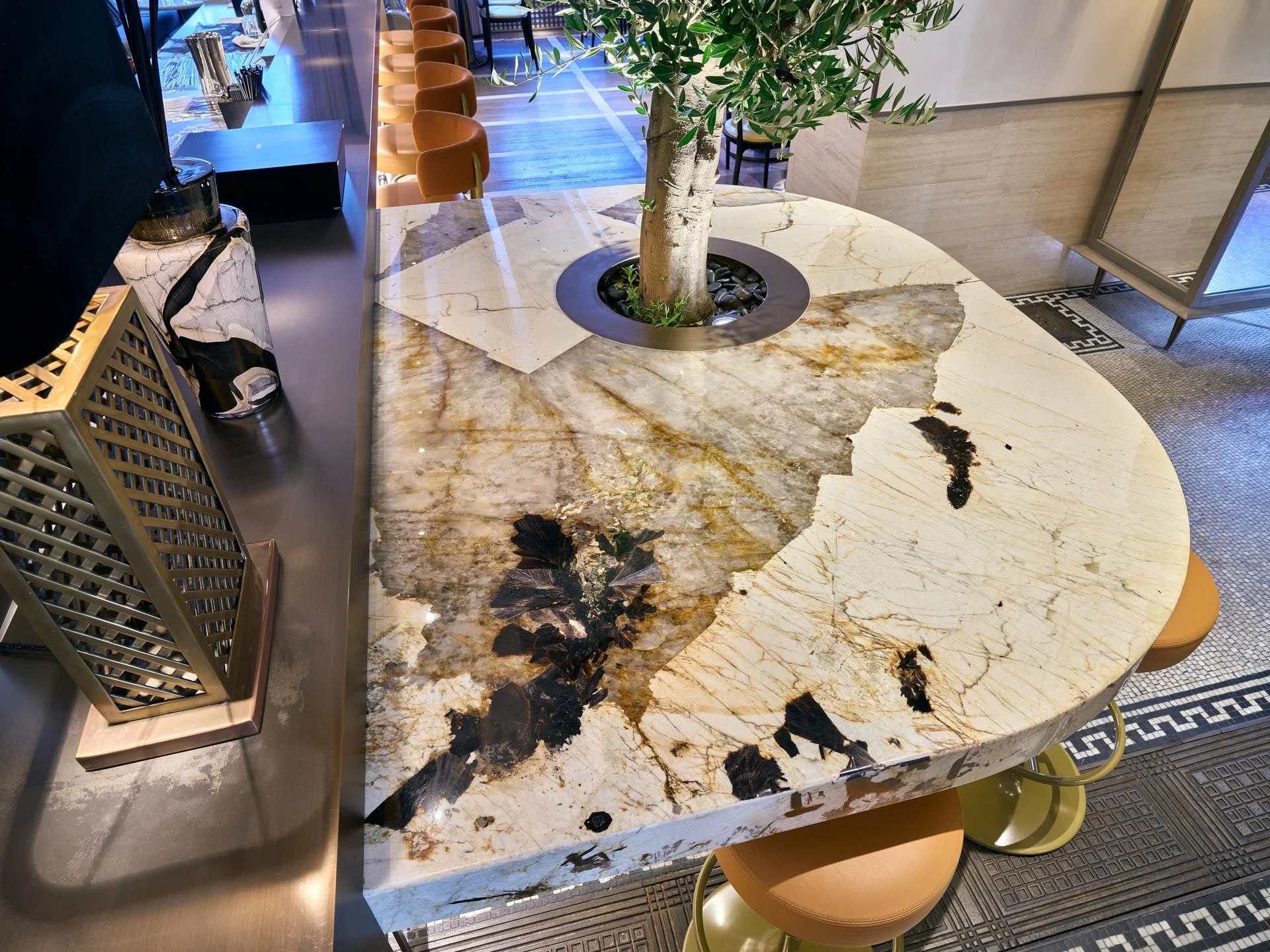 Overhead view of an expressive cream, gold and dark-veined stone table surrounding an olive tree.