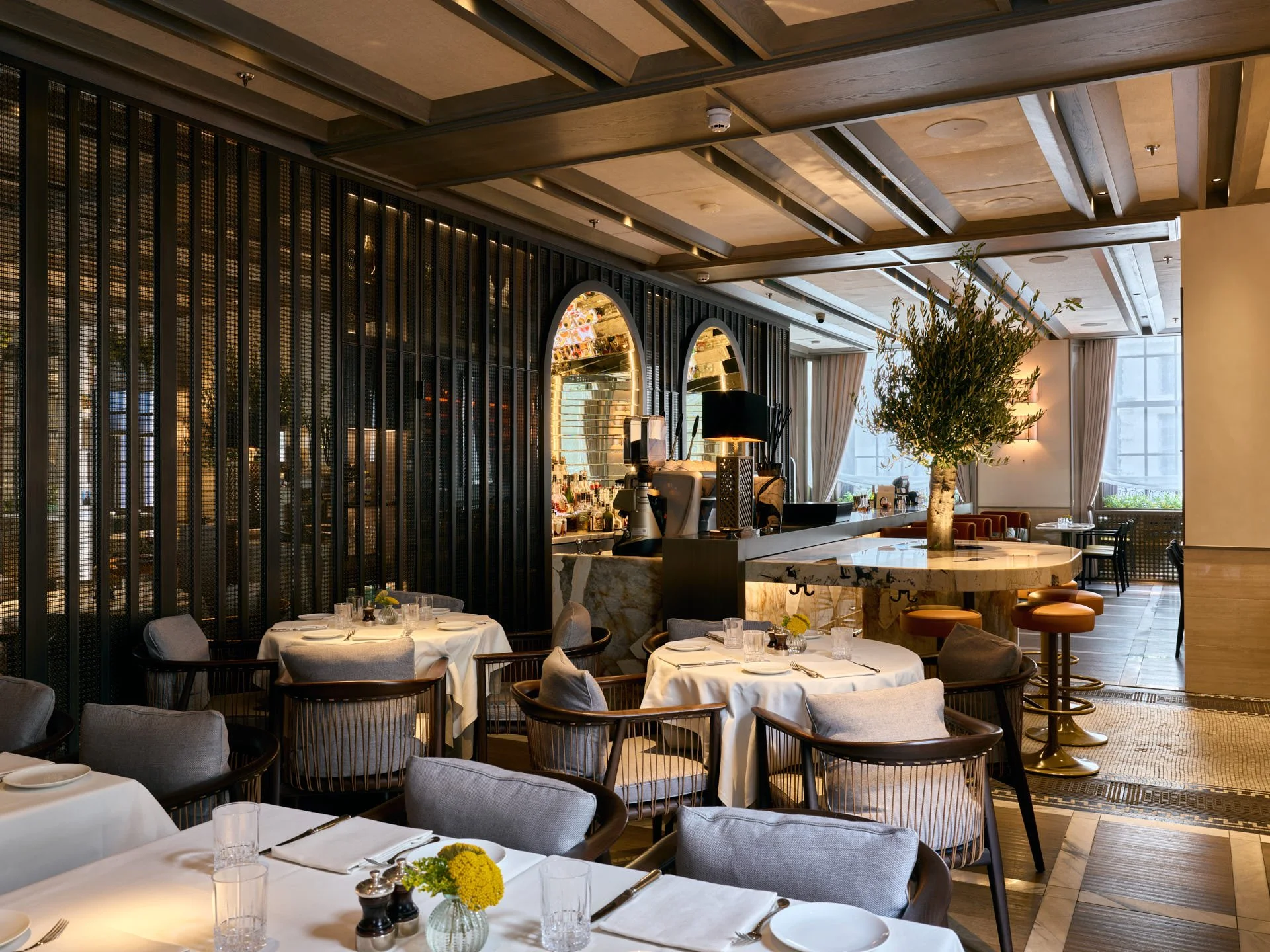 Wide view across set dining tables towards the stone bar and circular island at Paper Moon Restaurant.
