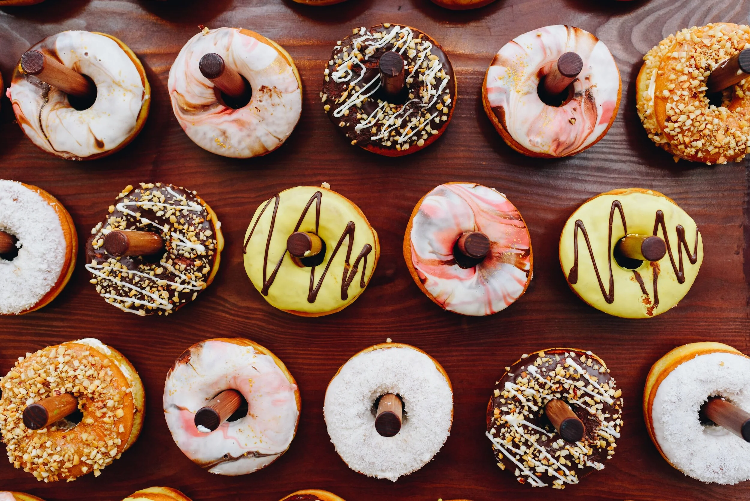 An assortment of decorated donuts arranged on a wooden surface, featuring various toppings and icing colors.