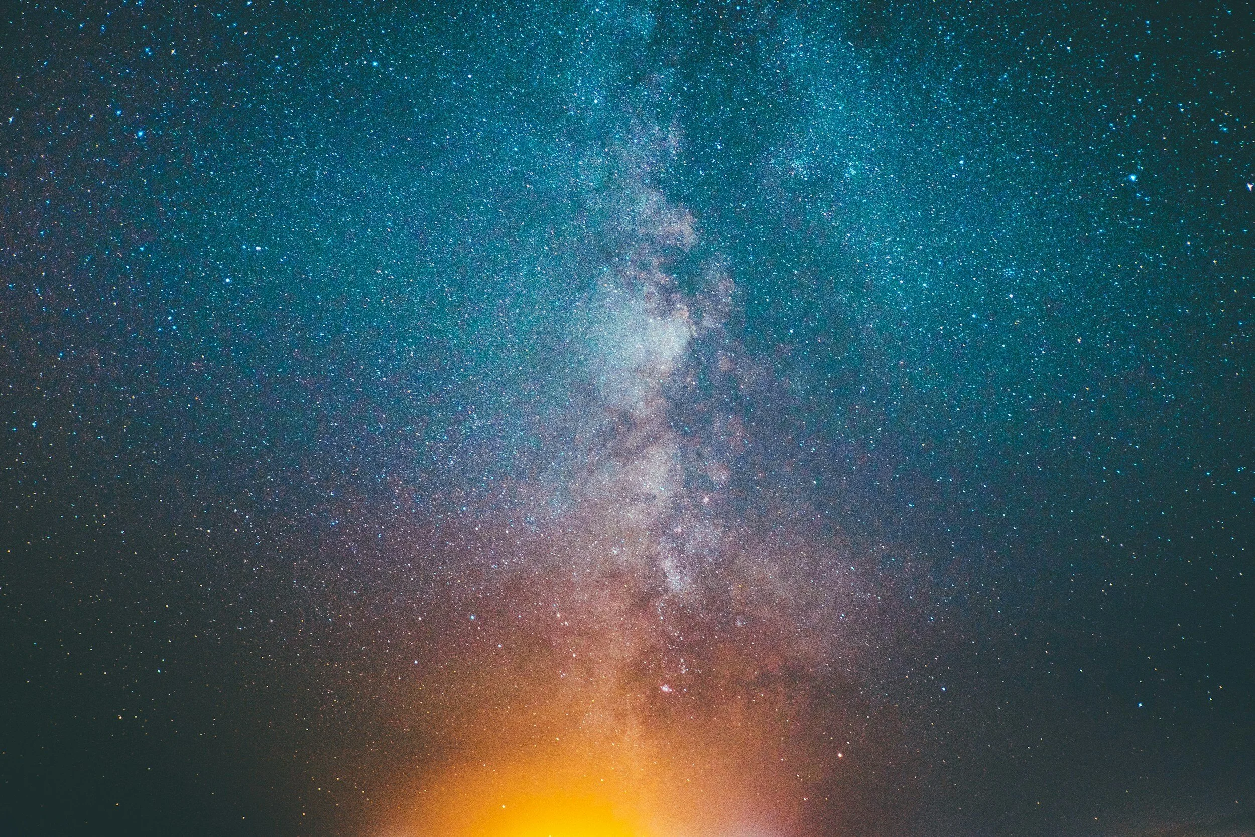 A star-filled night sky with the Milky Way galaxy visible, and a warm glow on the horizon.