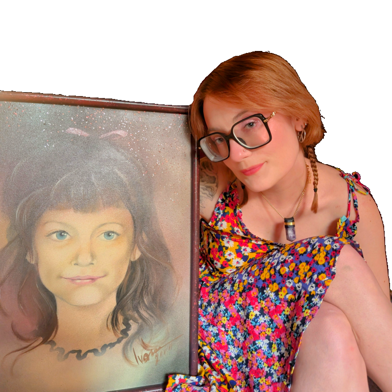 A woman with short red hair, glasses, and a colorful floral dress poses next to a framed portrait of a girl with dark hair and blue eyes.