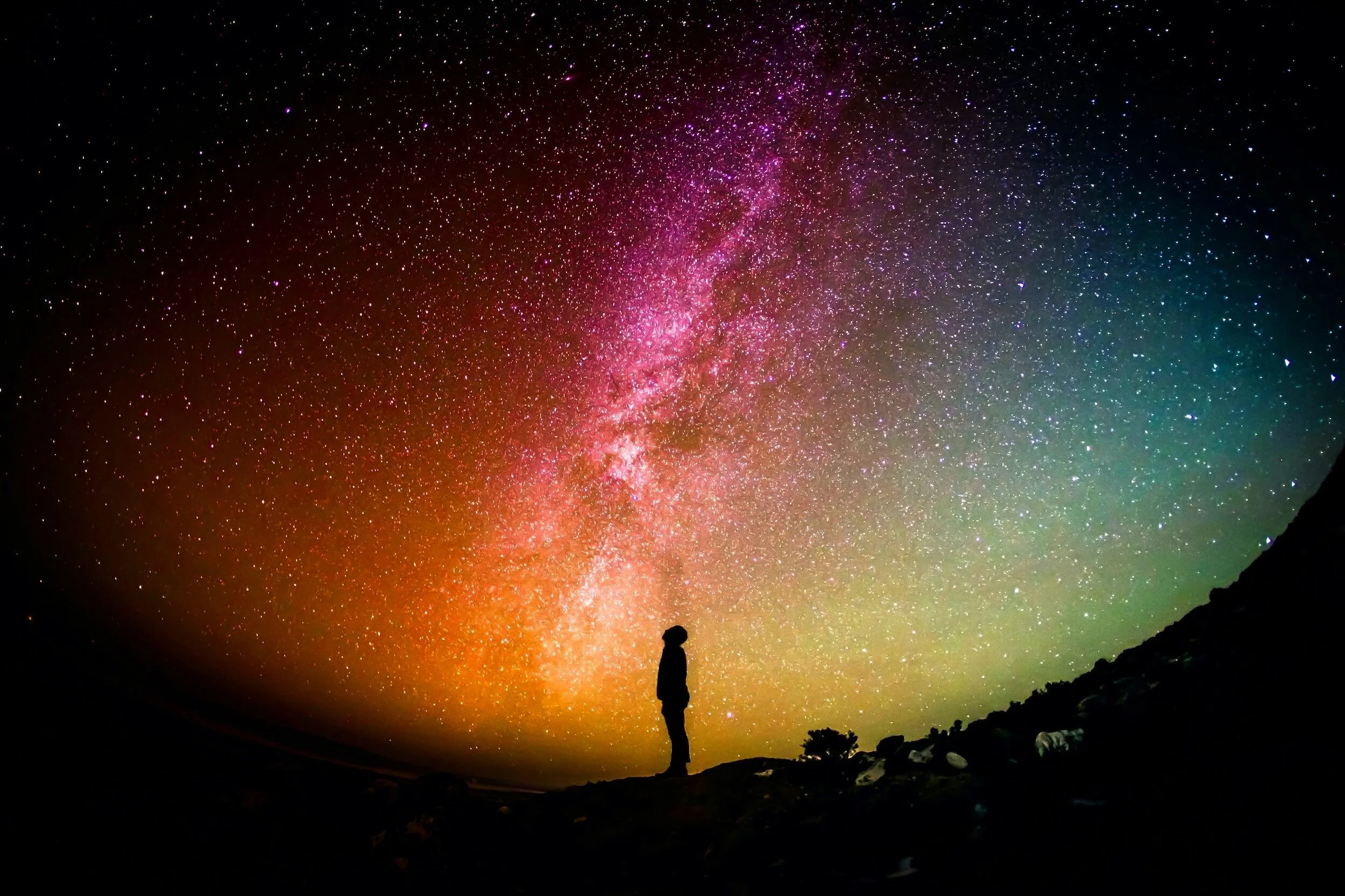 Person silhouetted against a colorful starry night sky with the Milky Way galaxy visible.