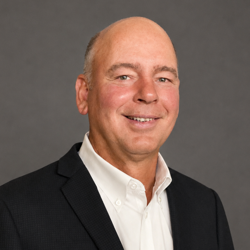Portrait of a bald man in a black blazer and white shirt smiling at the camera against a gray background.