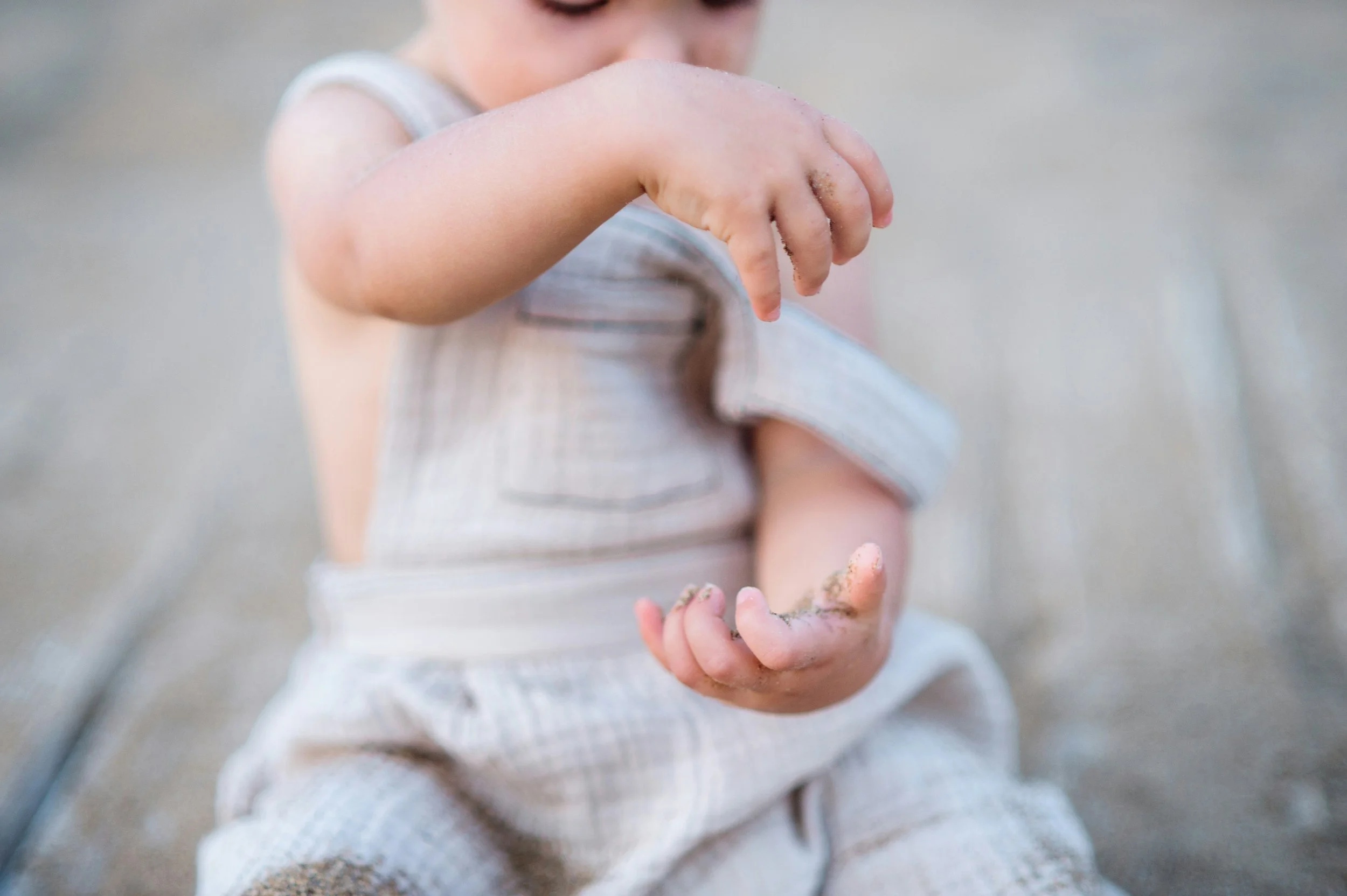 Close-up of a child's hand holding a handful of sand with dirt on the fingers, sitting on sandy ground.