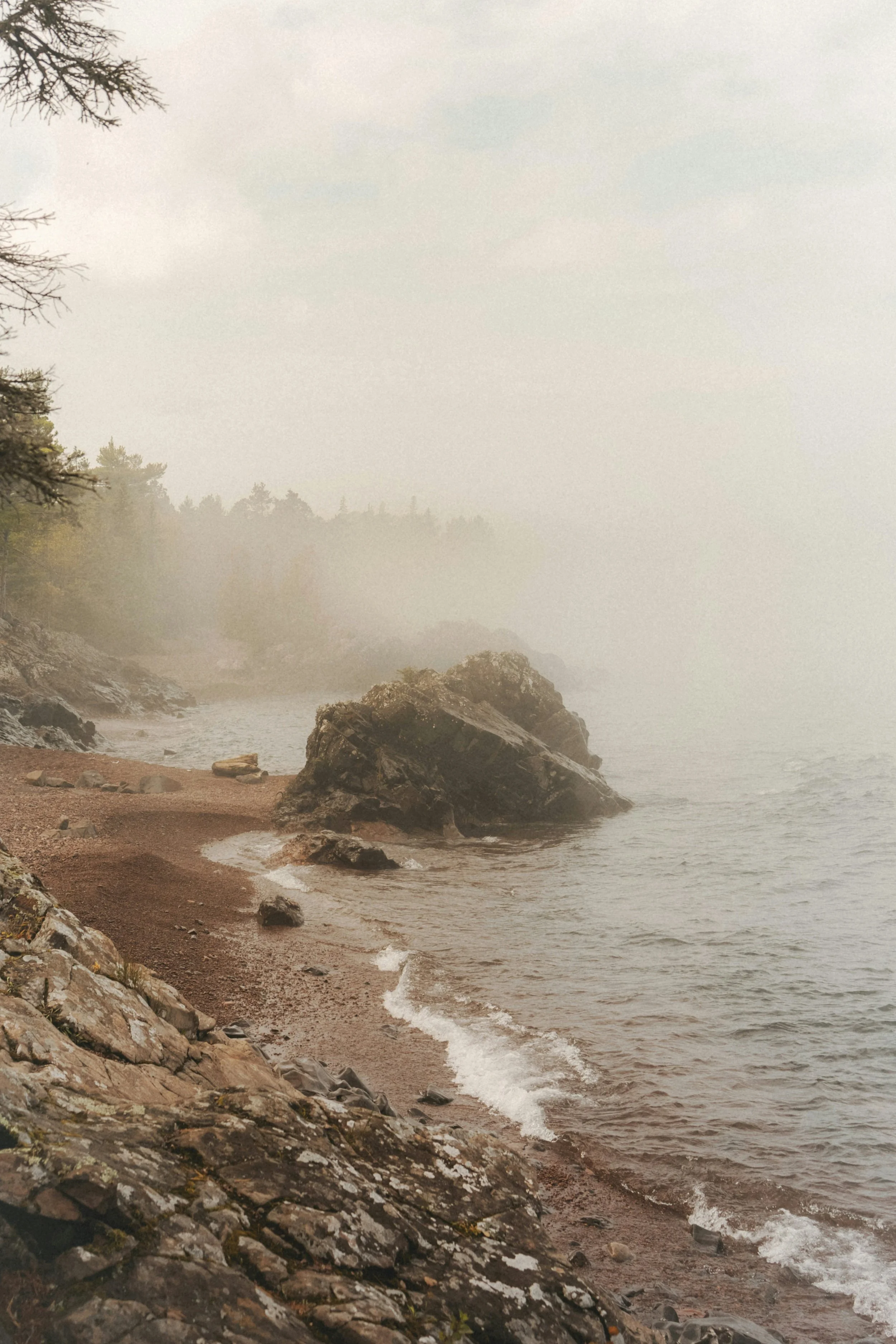 A foggy lakeside scene with rocks on the shore, trees in the background, and a misty atmosphere