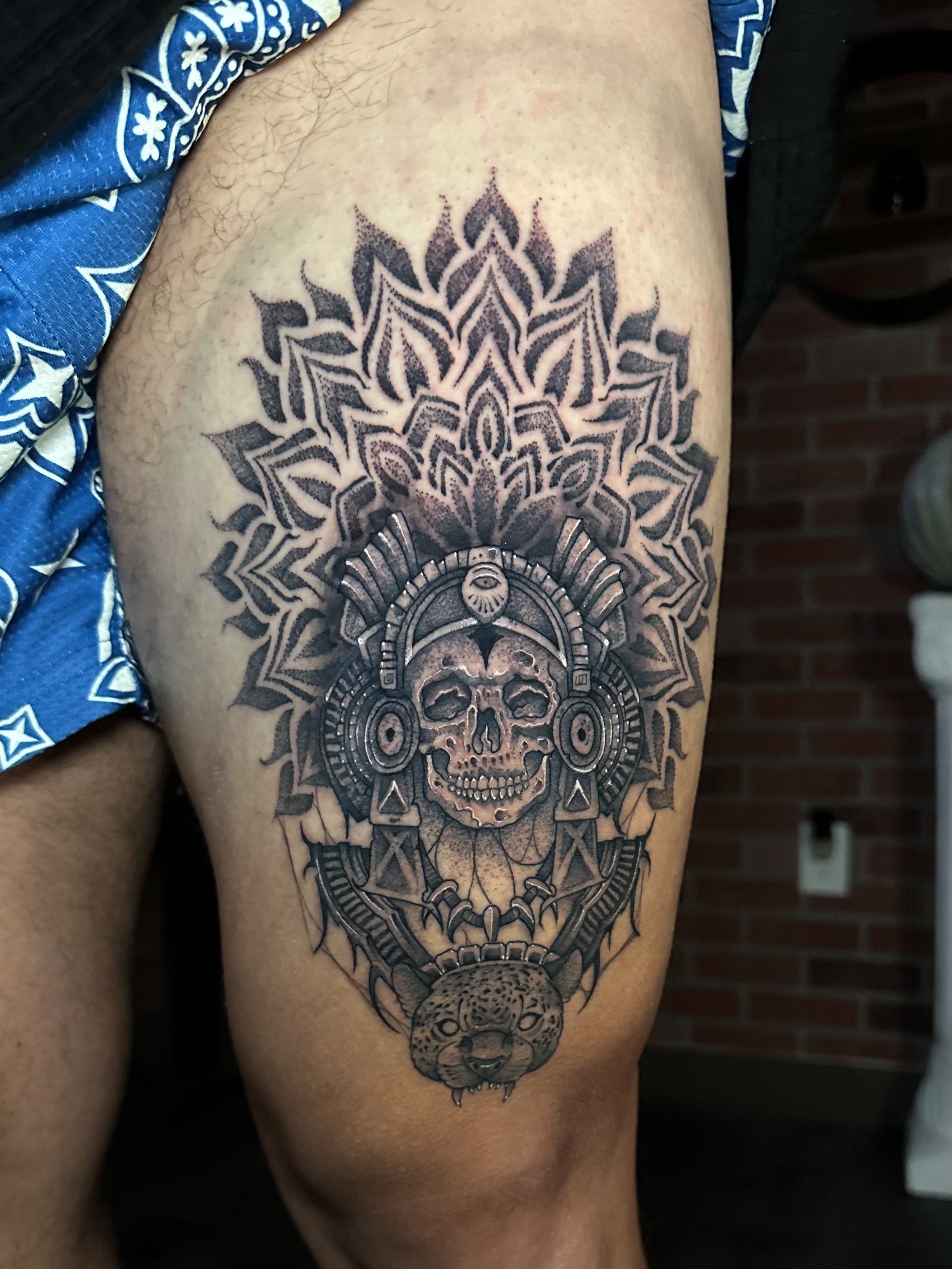 Black and grey thigh piece combining ornamental mandala, skull, and sacred geometry.