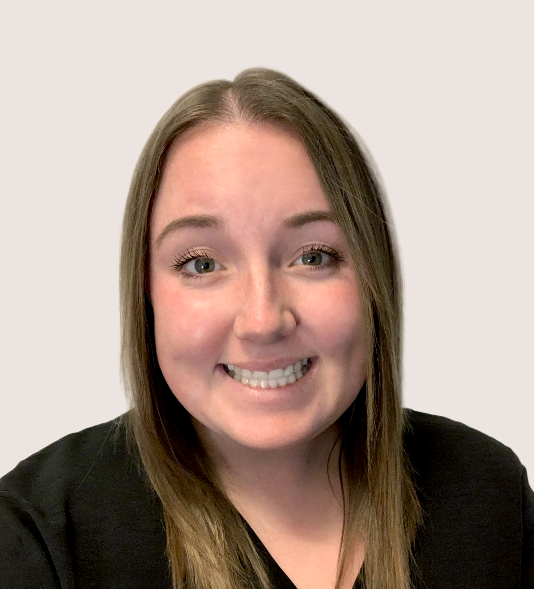 Close-up of a smiling young woman with long brown hair, wearing a black top, standing against a plain light background.
