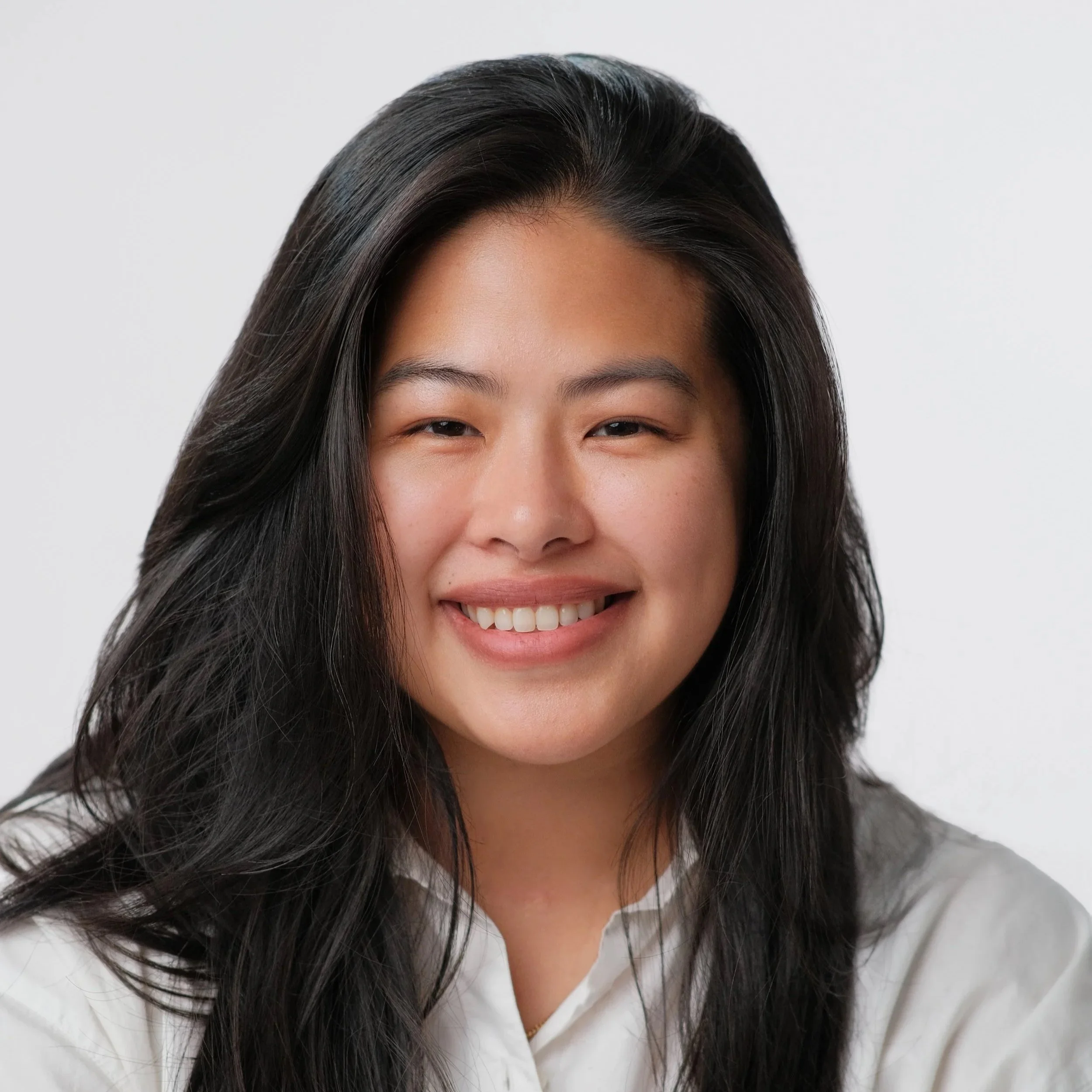A young woman with long brown hair smiling at the camera against a plain white background.
