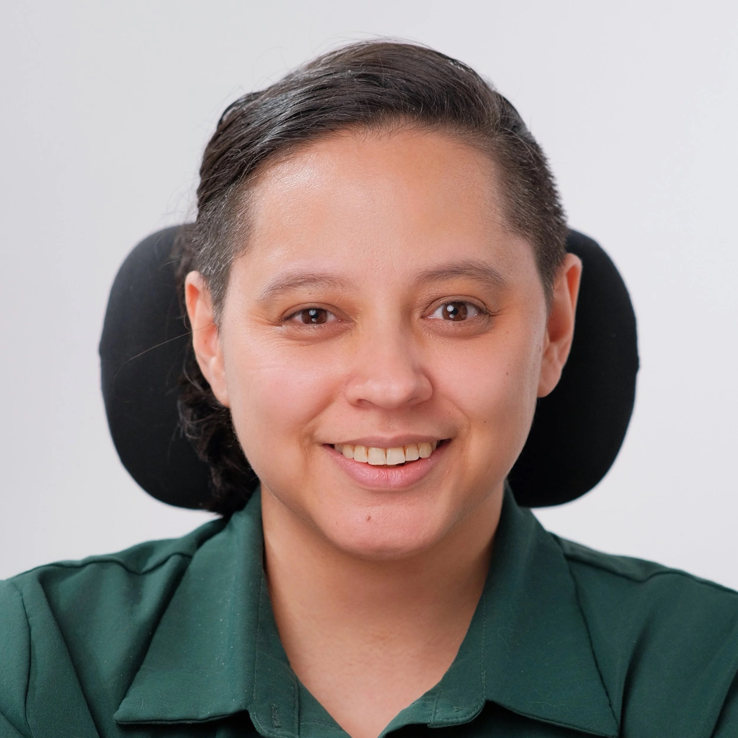 A smiling woman with long, wavy brown hair and wearing a green top, standing against a plain white background.