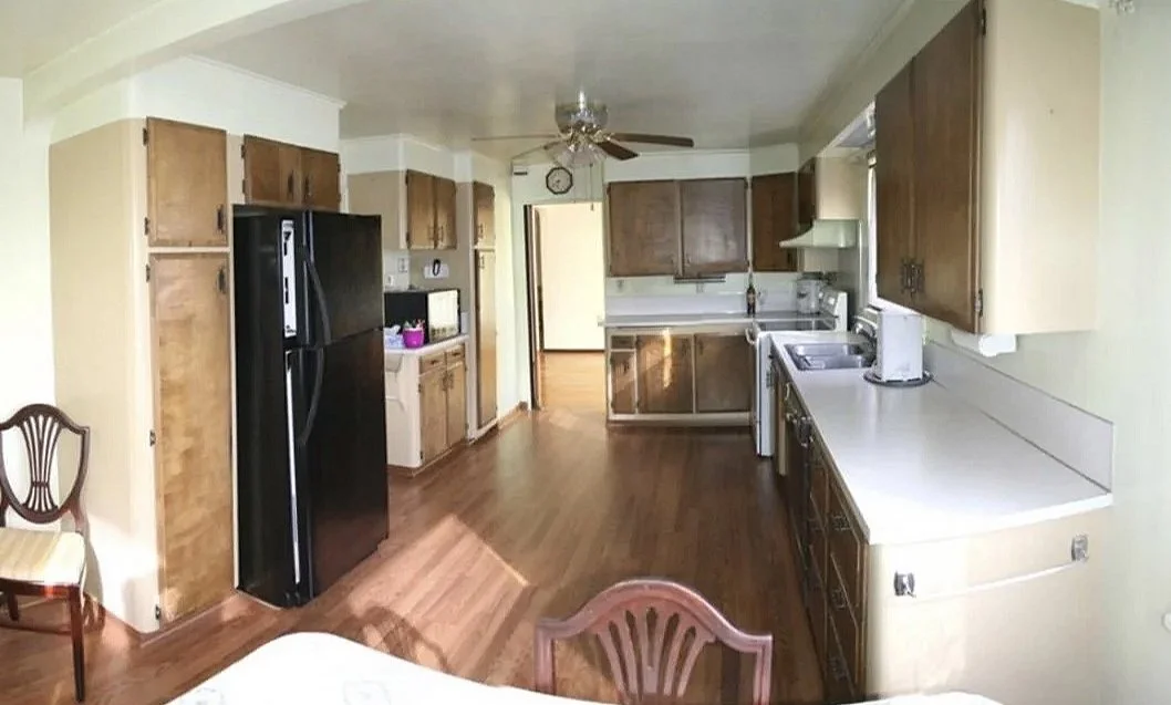 Kitchen with wooden cabinets, black refrigerator, white appliances, hardwood floor, ceiling fan, and yellow walls.
