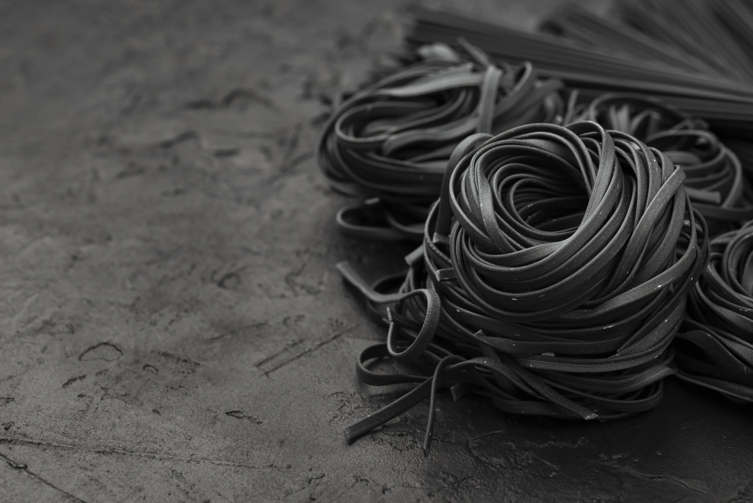 Close-up of black colored fettuccine pasta nests on a dark, textured surface.