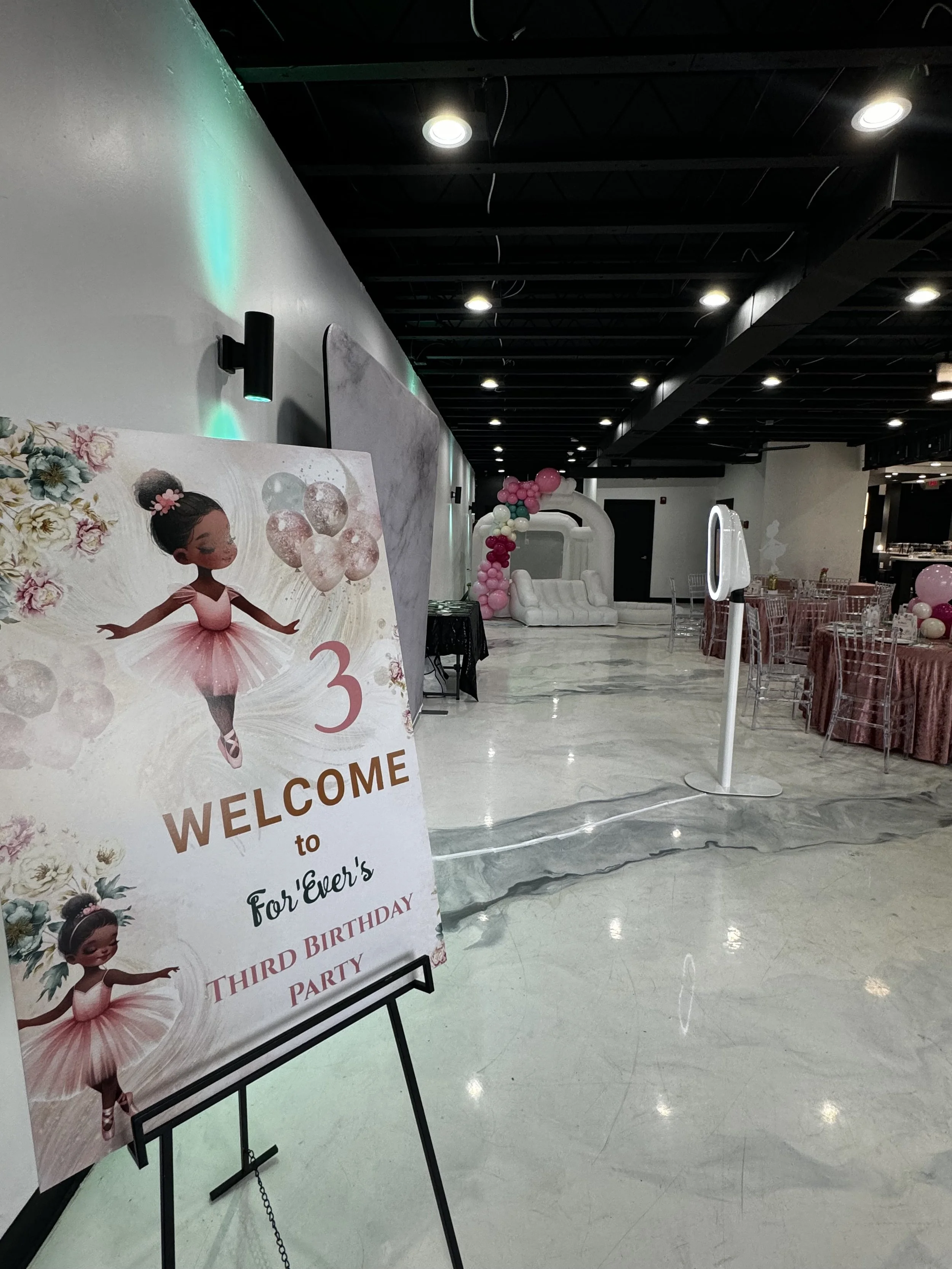 Decorated event space for a third birthday party with pink and white balloons and a sign featuring a ballerina girl and birthday message.