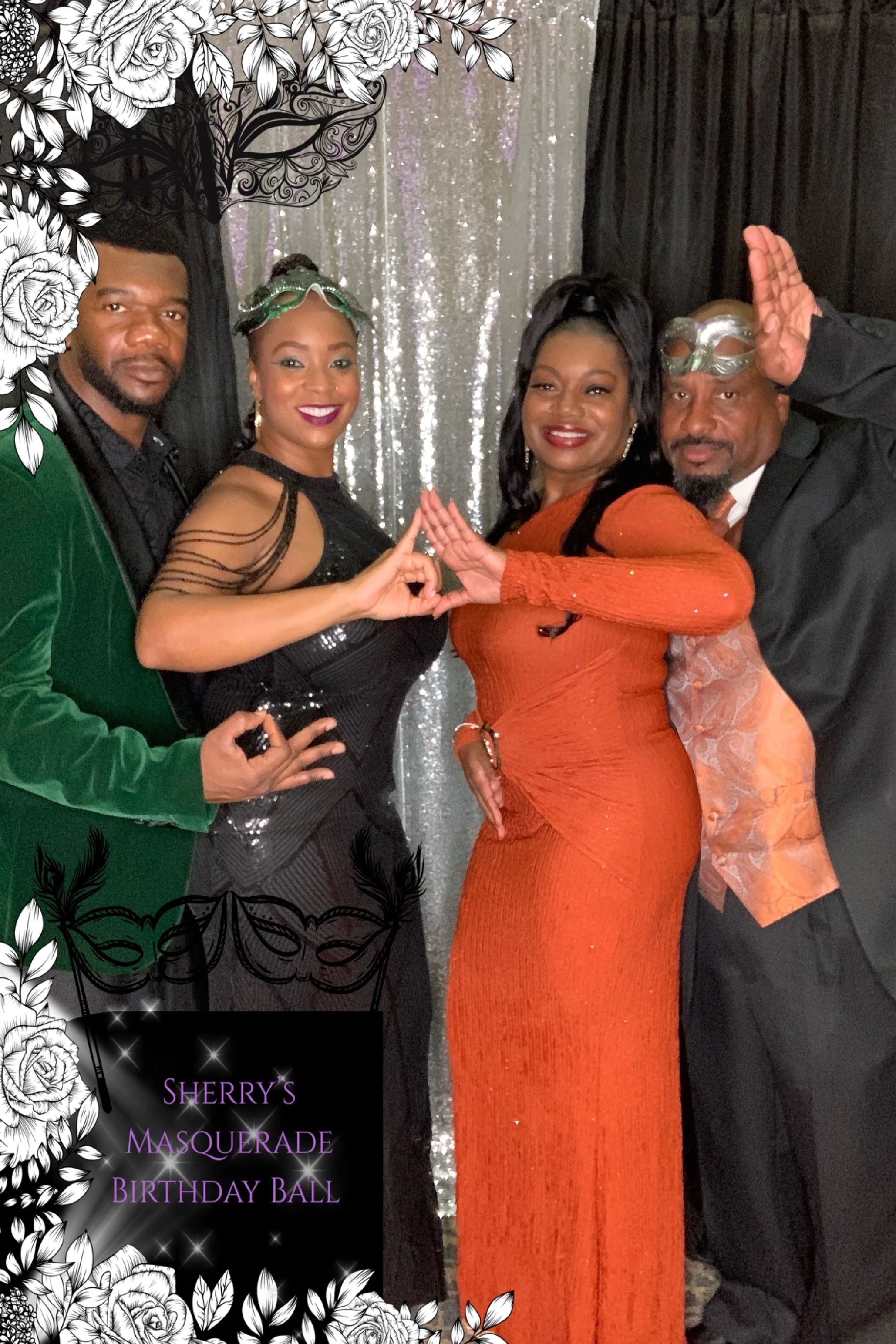 Four adults standing together at a masquerade birthday ball, with a silver sequin backdrop. One woman in an orange gown is in the center, flanked by a woman in a black dress with lace details, a man in a green velvet jacket, and another man in a blac