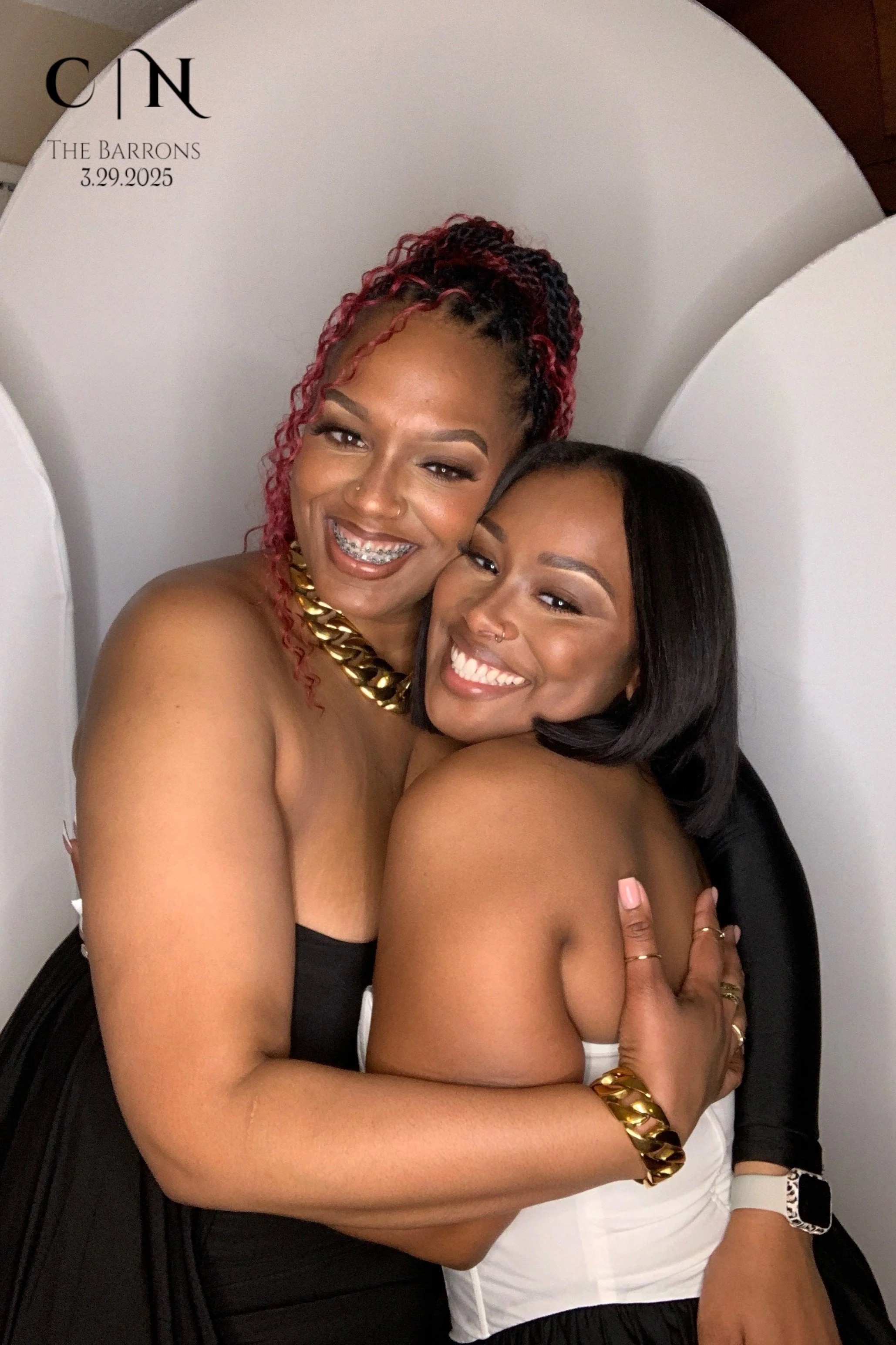 Two women hugging and smiling at a photo booth, with white and black backgrounds, on March 29, 2025, at The Barrons event.