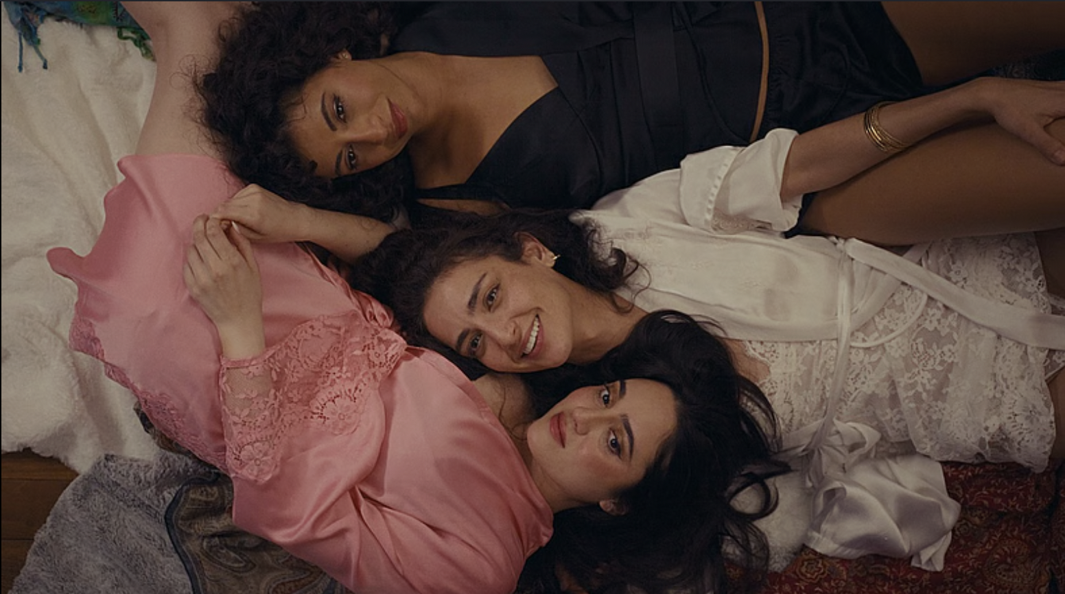 Three women lying on the floor, closely positioned together, smiling and relaxing indoors.
