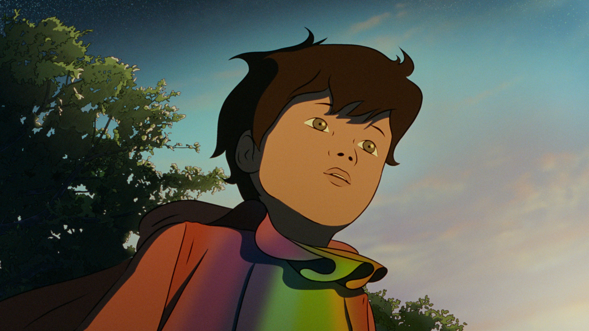 A young boy with dark hair and tan skin looks upward with a thoughtful expression. He is outdoors with trees and a colorful sky in the background, wearing a multicolored rainbow jacket with a black scarf.