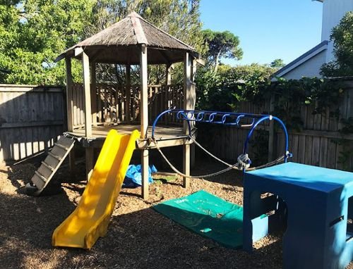 Outdoor play area with a wooden treehouse, slide and swings