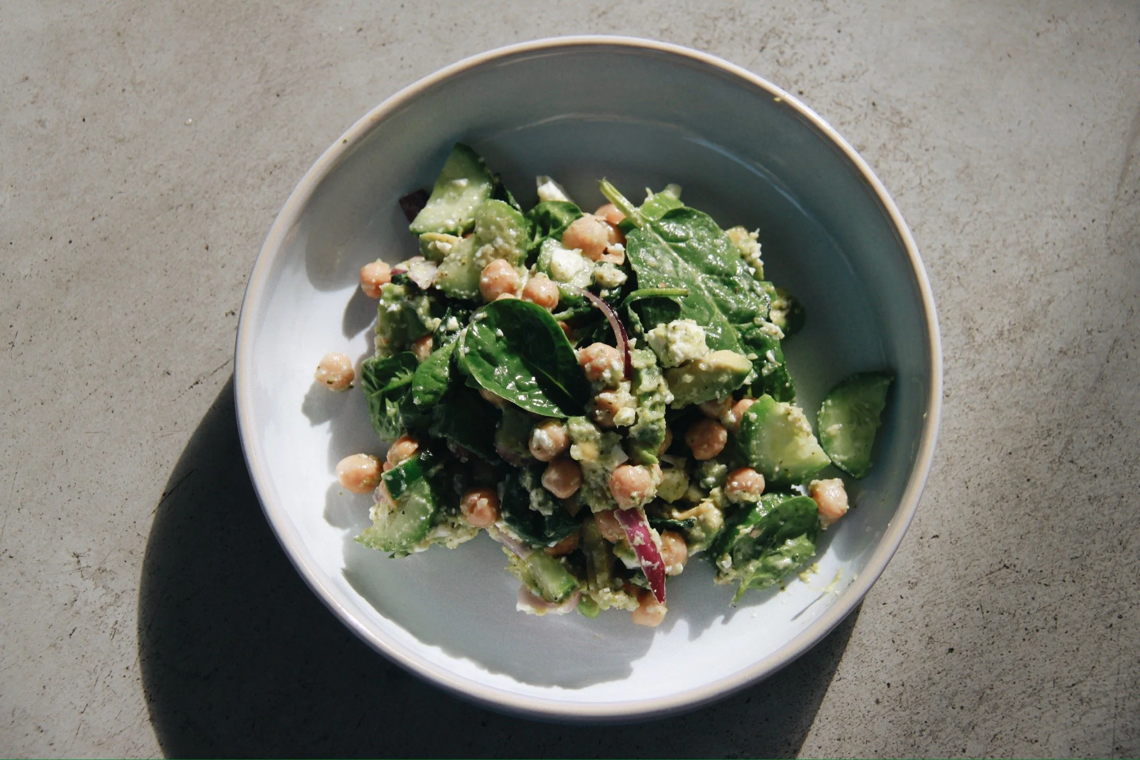 Gemüsesalat mit Gurken, Spinat, Salatblättern und Kichererbsen in einer blauen Schüssel
