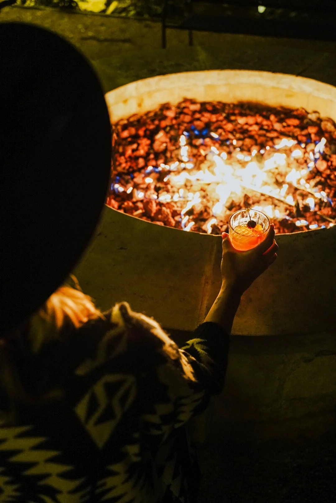 woman sitting by firepit with cocktail
