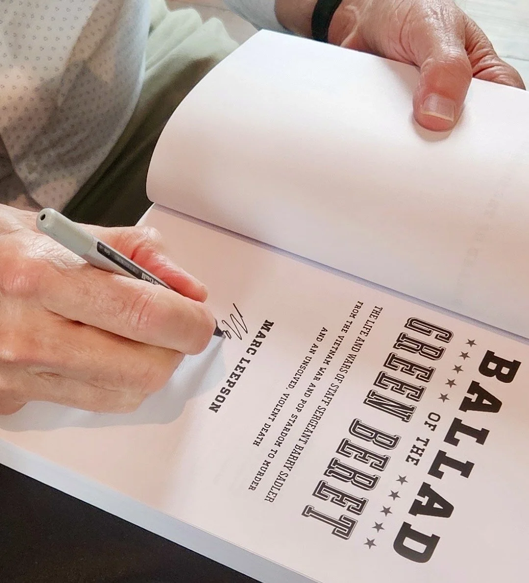 Close-up of a person signing a certificate or document titled 'Battle of the Beered.' The person is using a black marker and holding a sheet of paper. The person's hands are visible, and they are wearing a light-colored shirt.