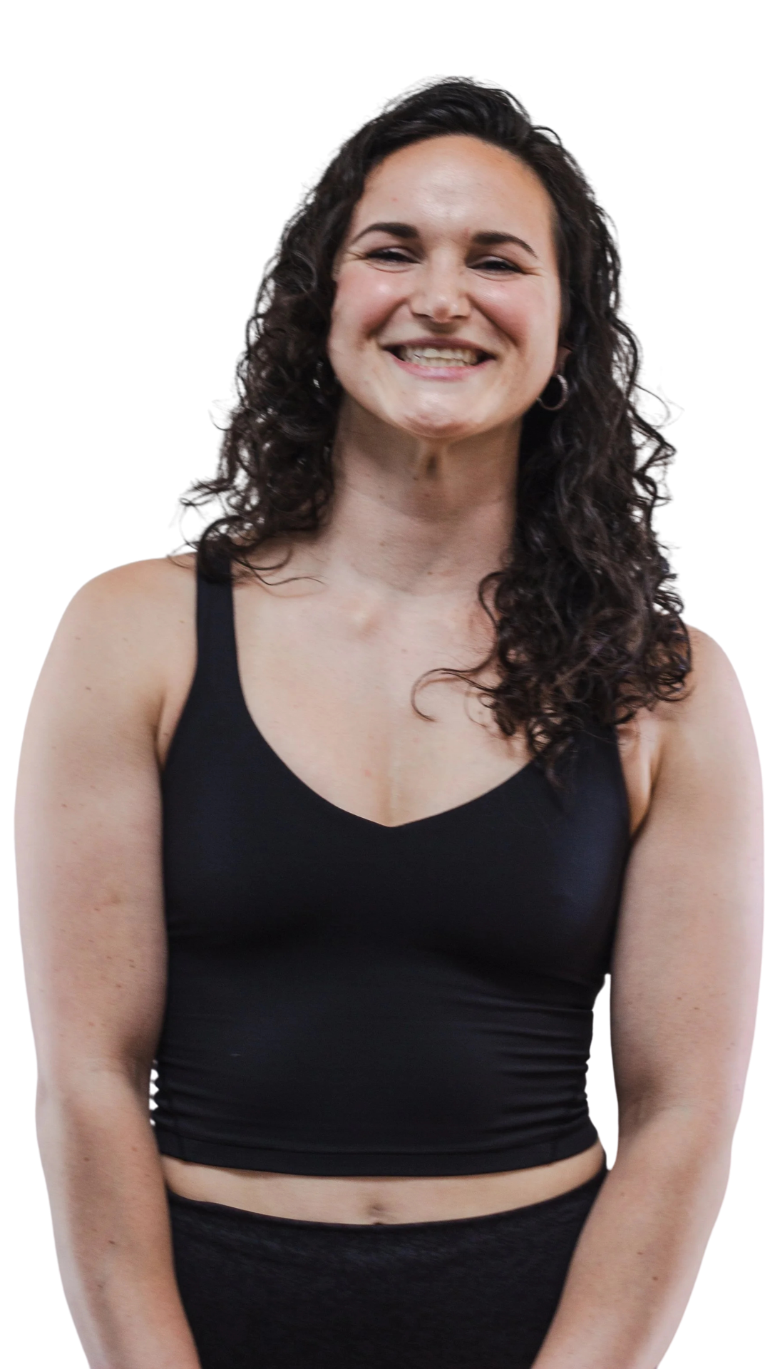 A woman with curly dark hair smiling, wearing a black sports bra and matching black bottoms, standing against a plain background.